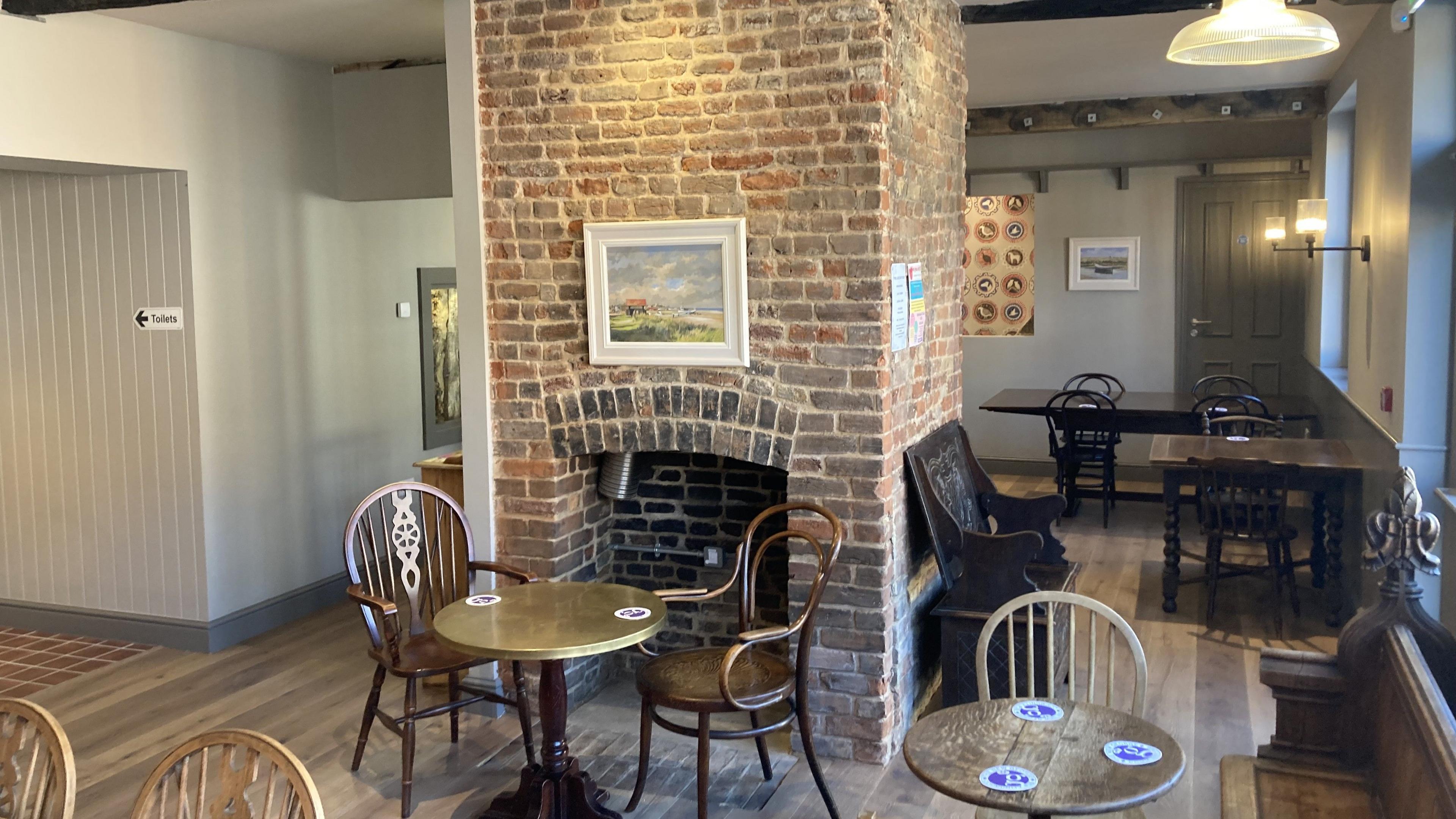The inside of a pub features empty tables and chairs with beer mats on the tables and artwork on the walls.