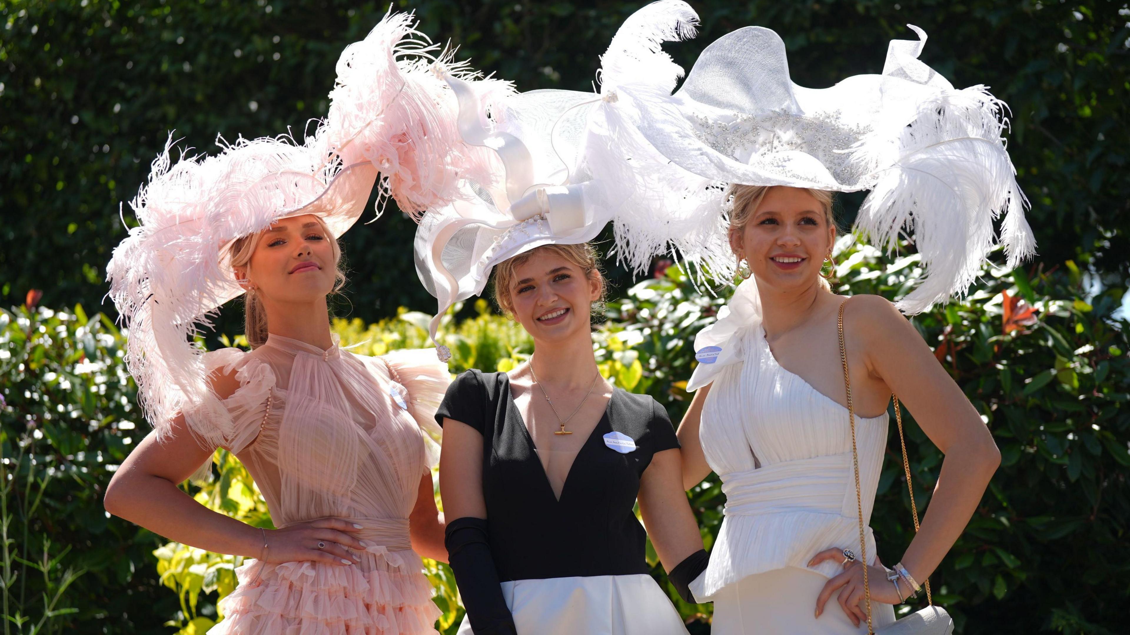 Three white blonde women pose for a photo wearing large white hats