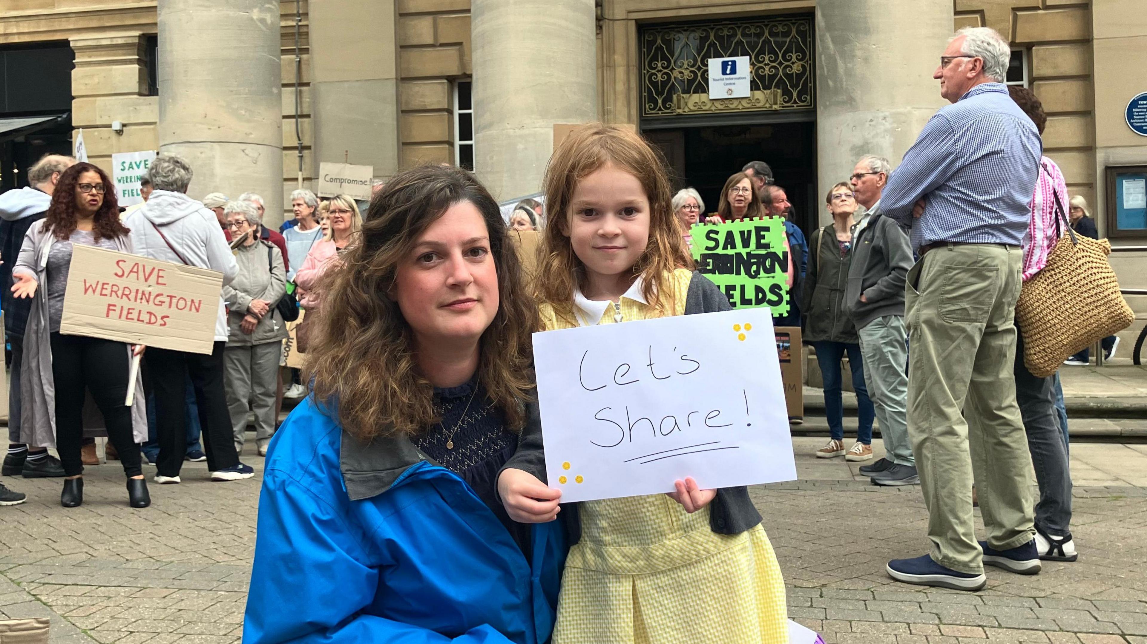 Nyree Ambarchian and her daughter smile directly at the camera, and hold a piece of paper reading "Let's share!"