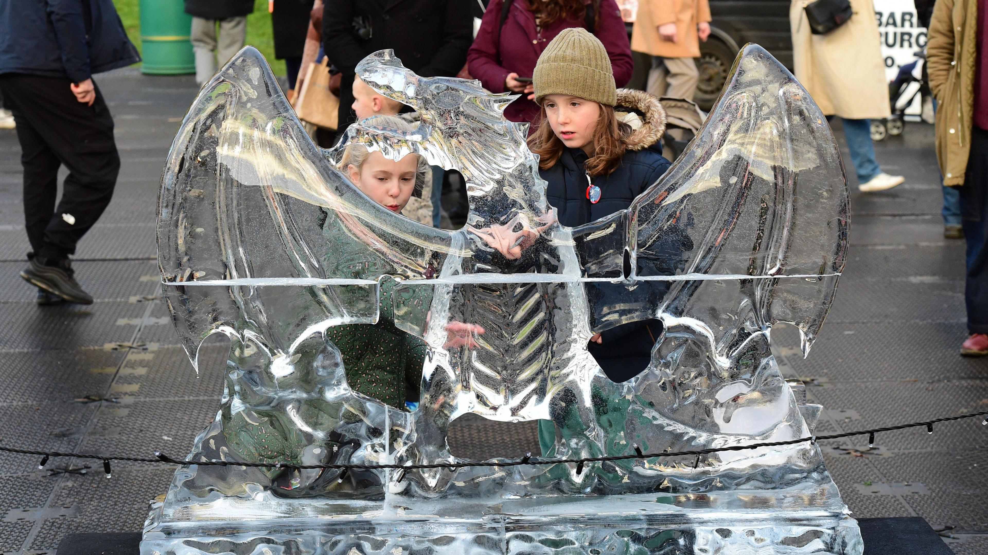 Two children standing behind one of last year's ice sculptures in the form of a dragon.