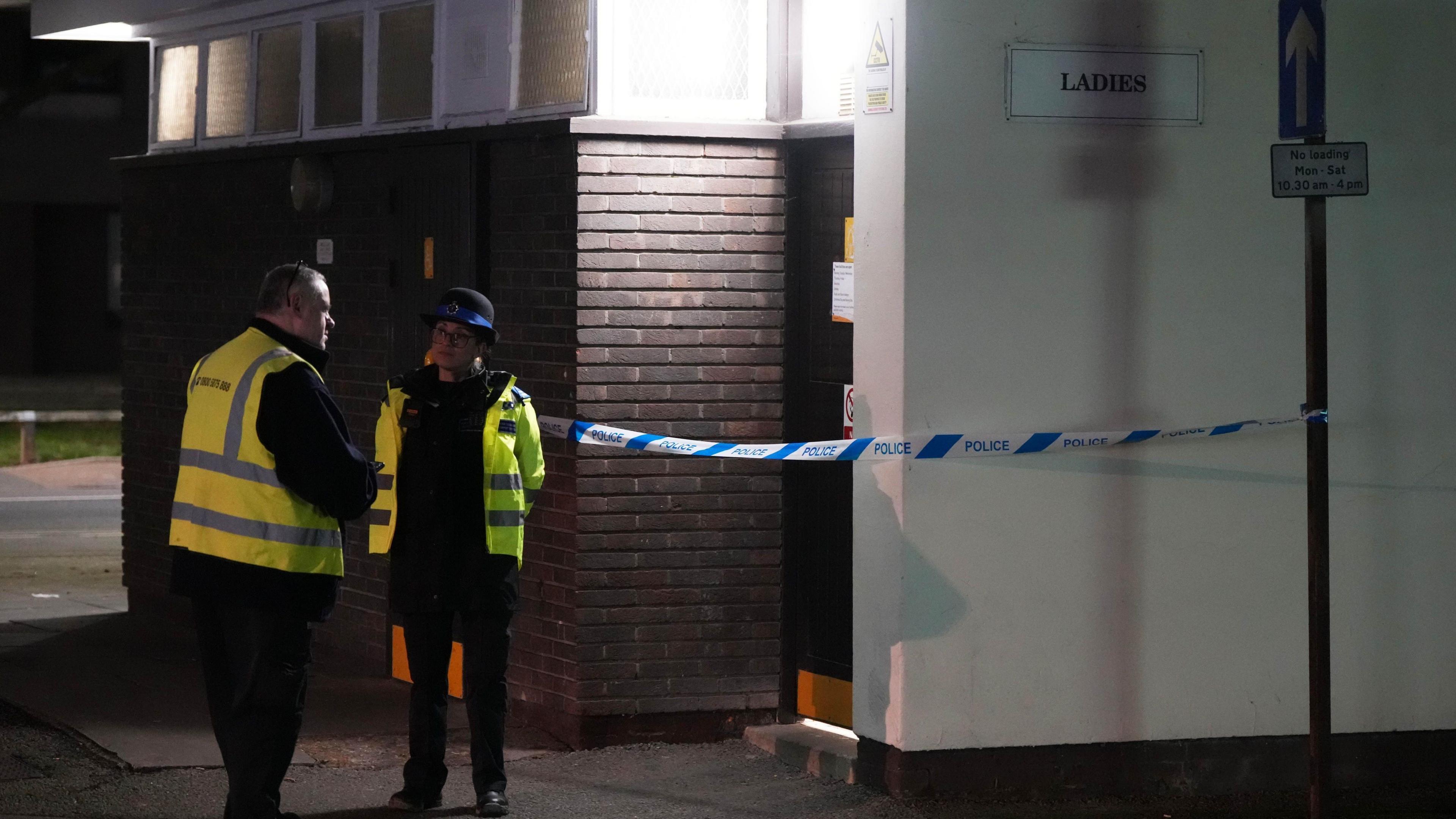 A police officer and a man in high-vis vest outside a public toilet at night