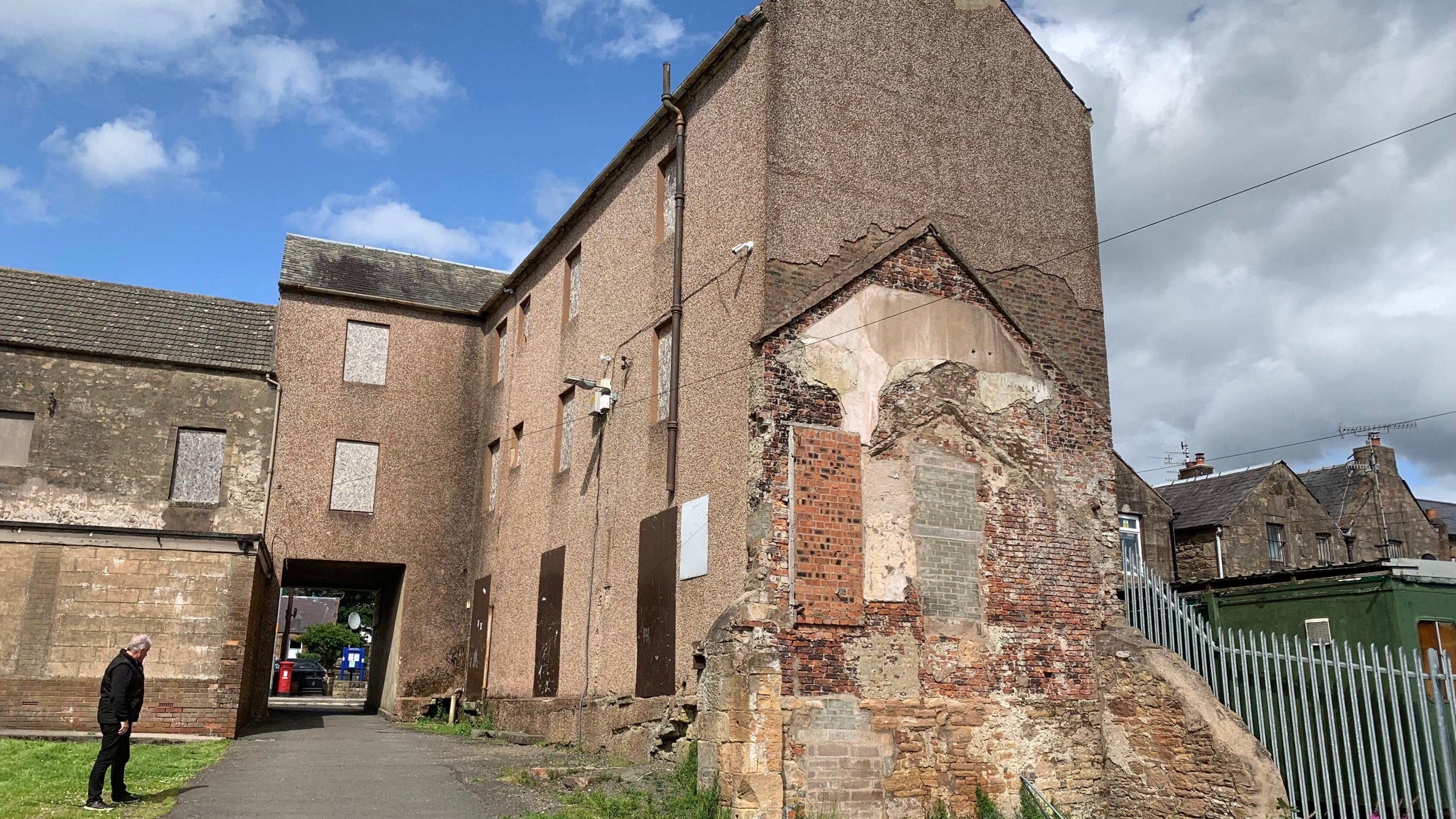 A rear view of a derelict put with open brickwork and a metal fence beside it