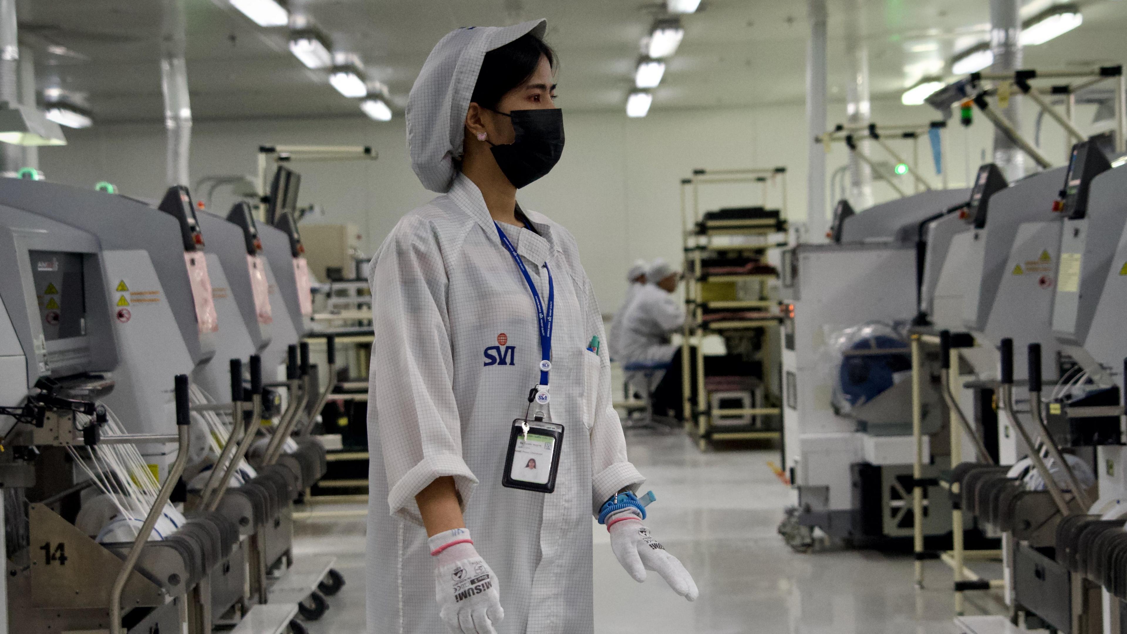 A worker in overalls at an electronics factory between rows of machines
