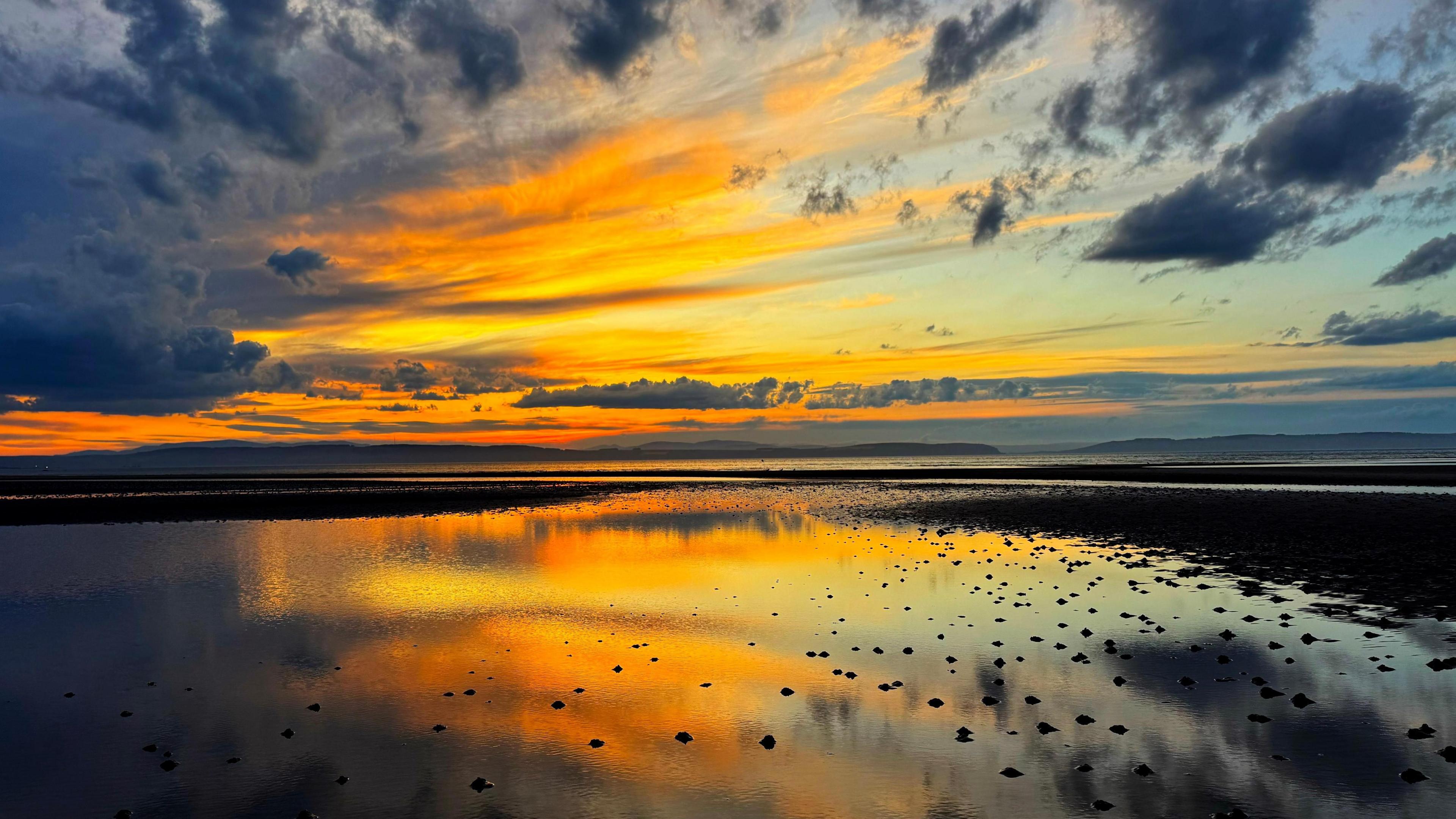 Sun rises and streams through wispy cloud over a beach
