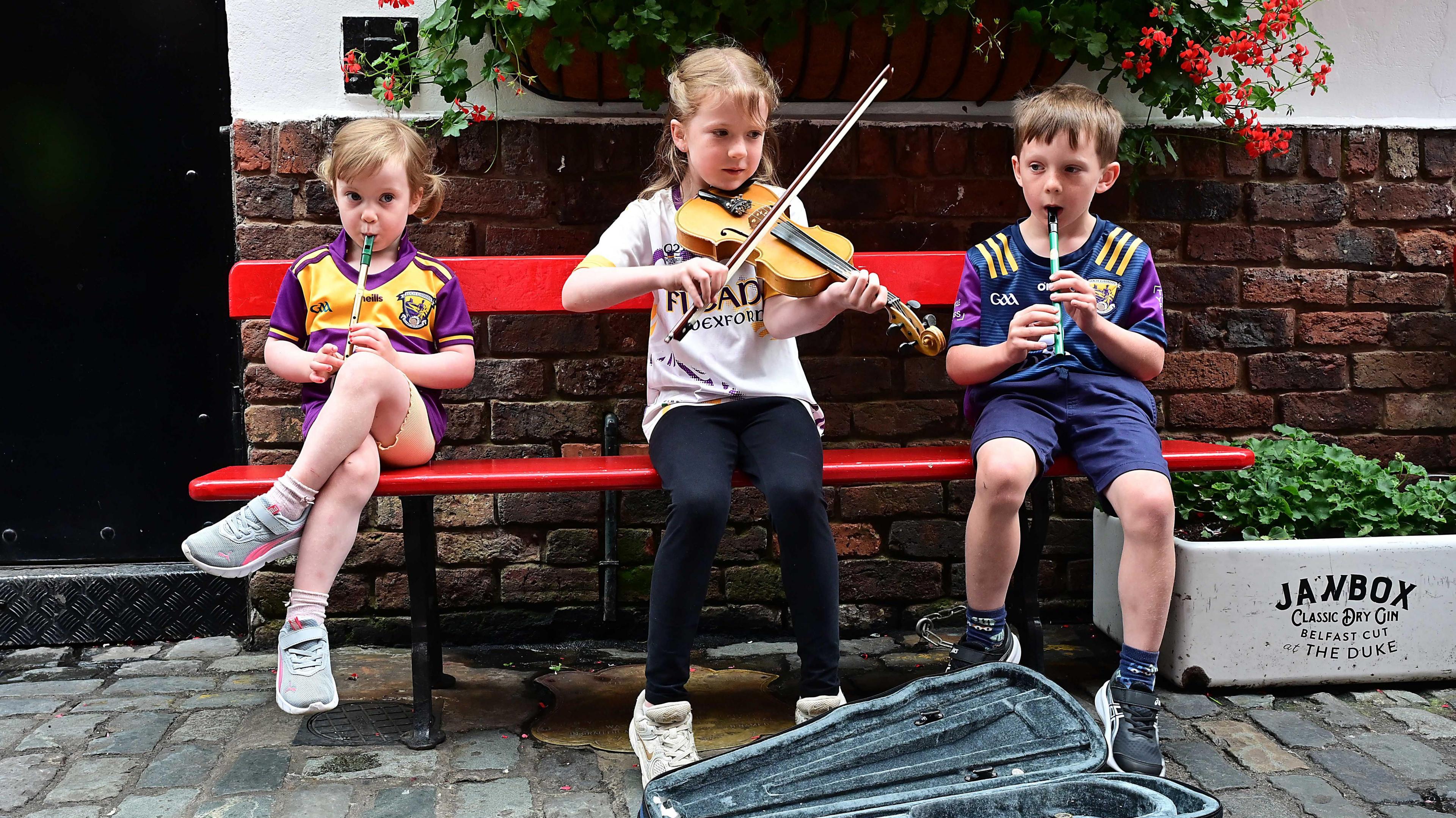 Three children. Two boys playing tin whistle, with a girl in the middle playing a violin.