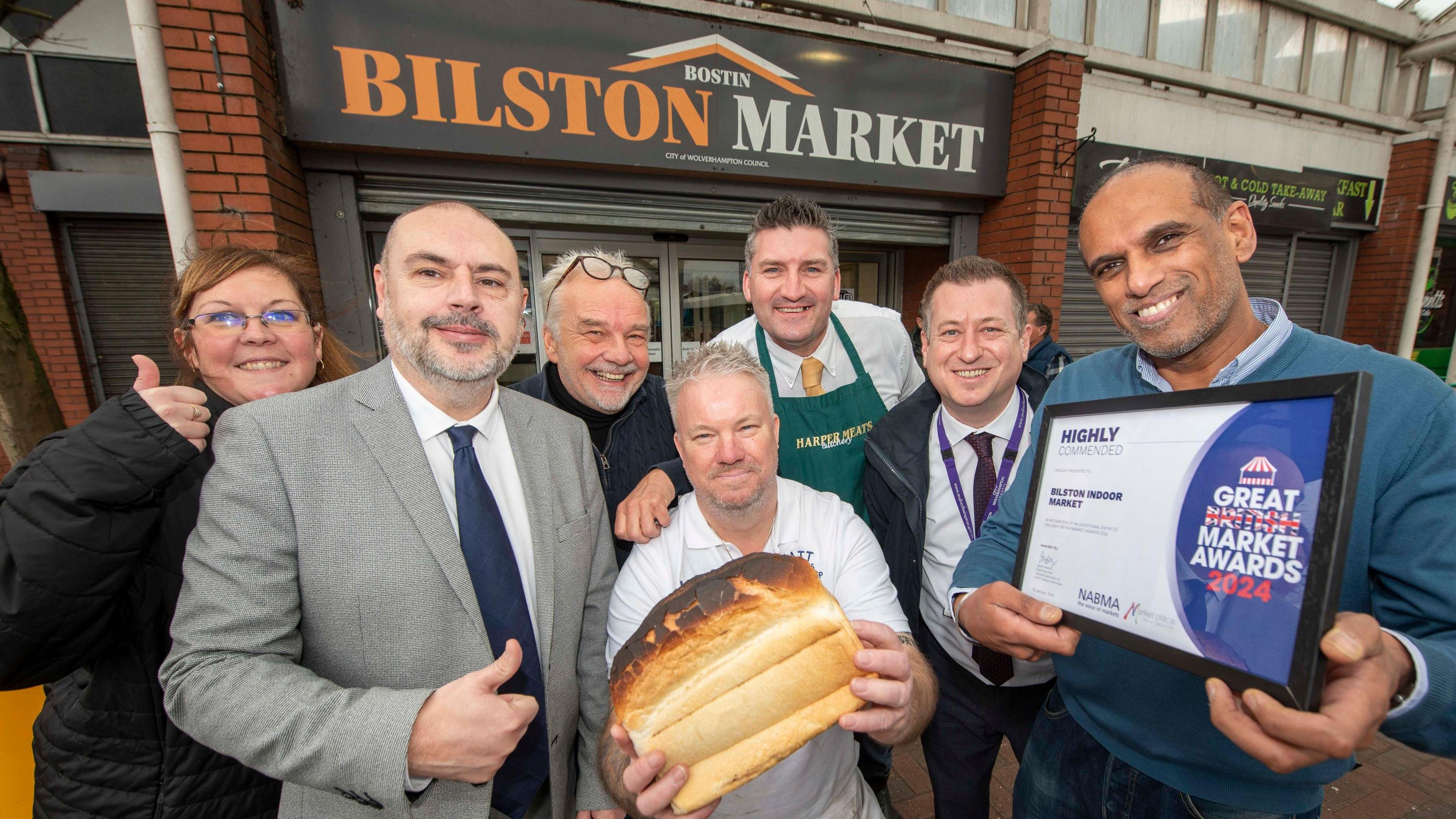 People celebrate with the award and a loaf of bred in the indoor market