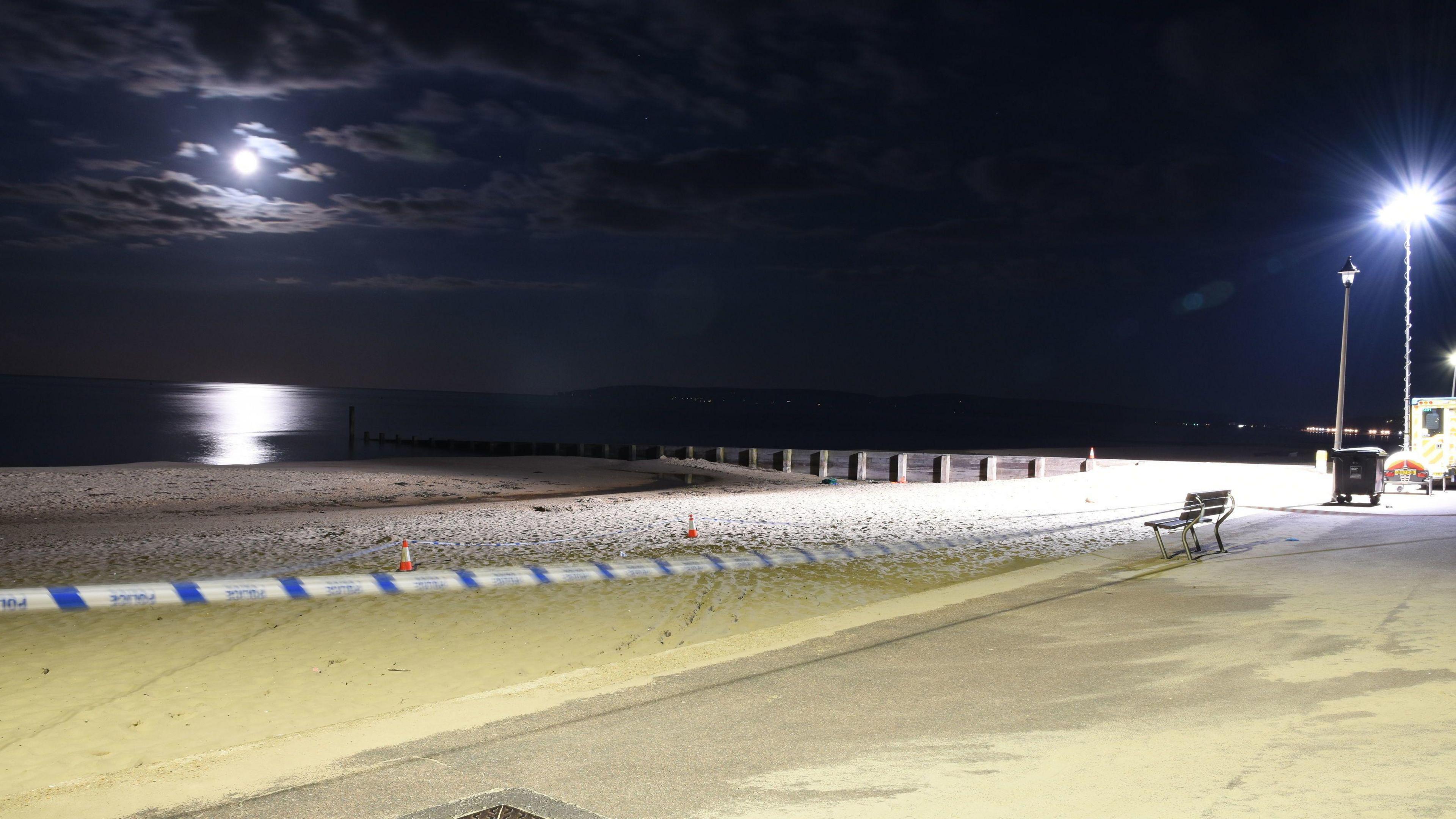 A view of Durley Chine beach on the night of 24 May 2024, showing the full moon and its reflection on the water. Police tape is stretched across the sand.