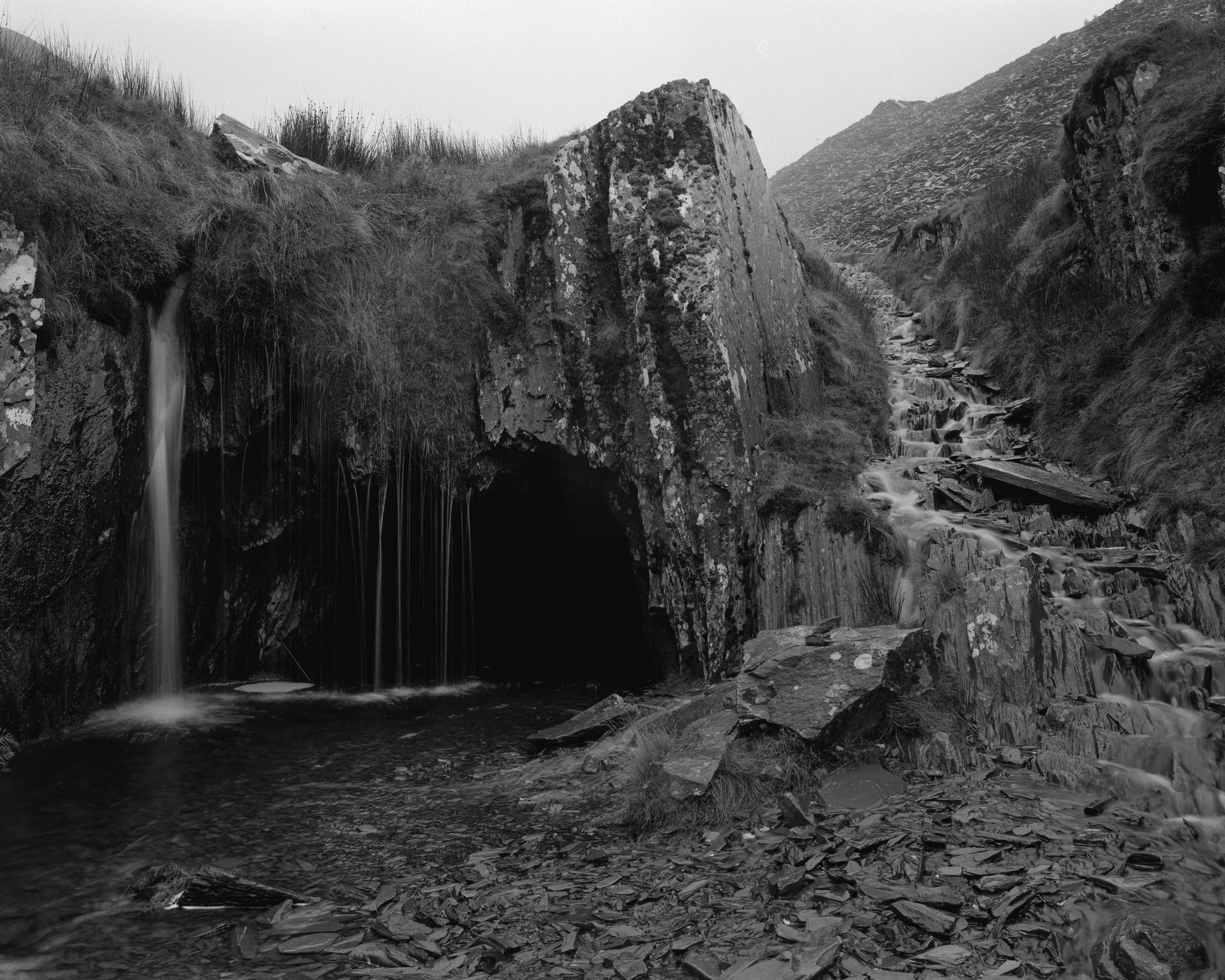 Kyle's black and white photograph of a craggy grey hillside with water creating a natural pool below. Beside the water are piles of slate.