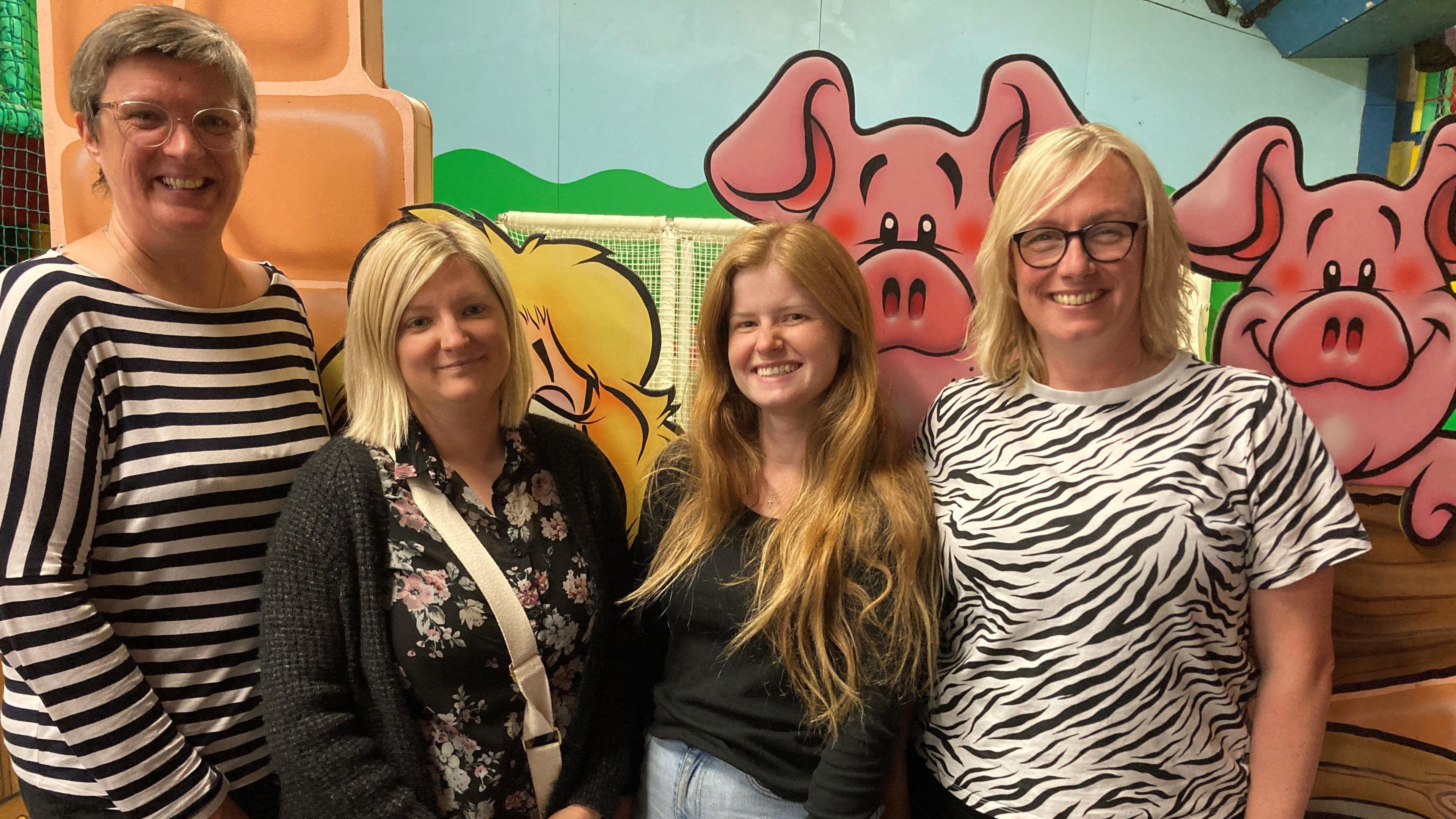 Four women standing in front of a farmyard background in a children's play barn.