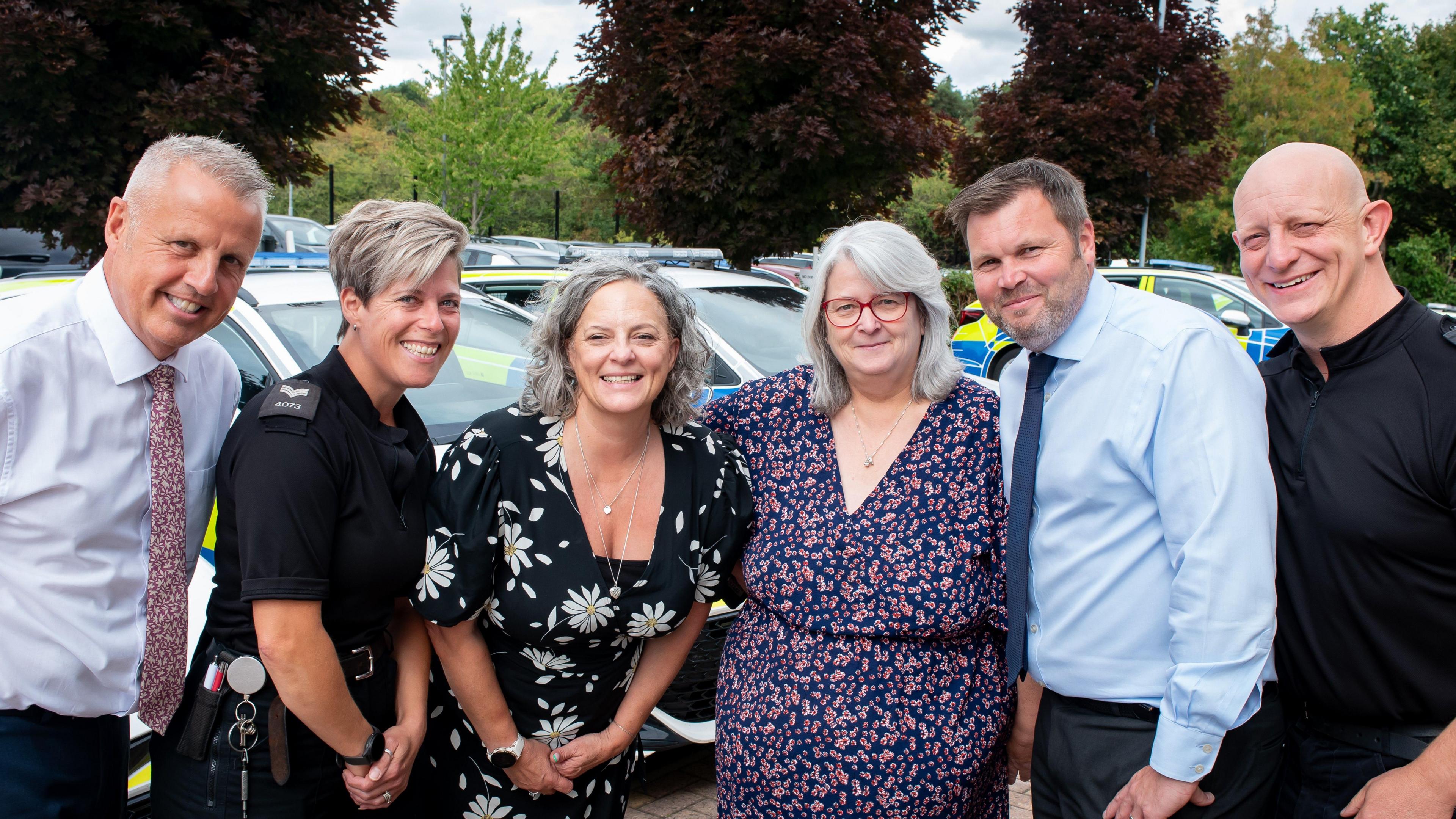Six police staff members line up for the camera, shoulder-to-shoulder. The group is made up of three men and three women. One of the women is in a police uniform while the other five are in smart casual clothes