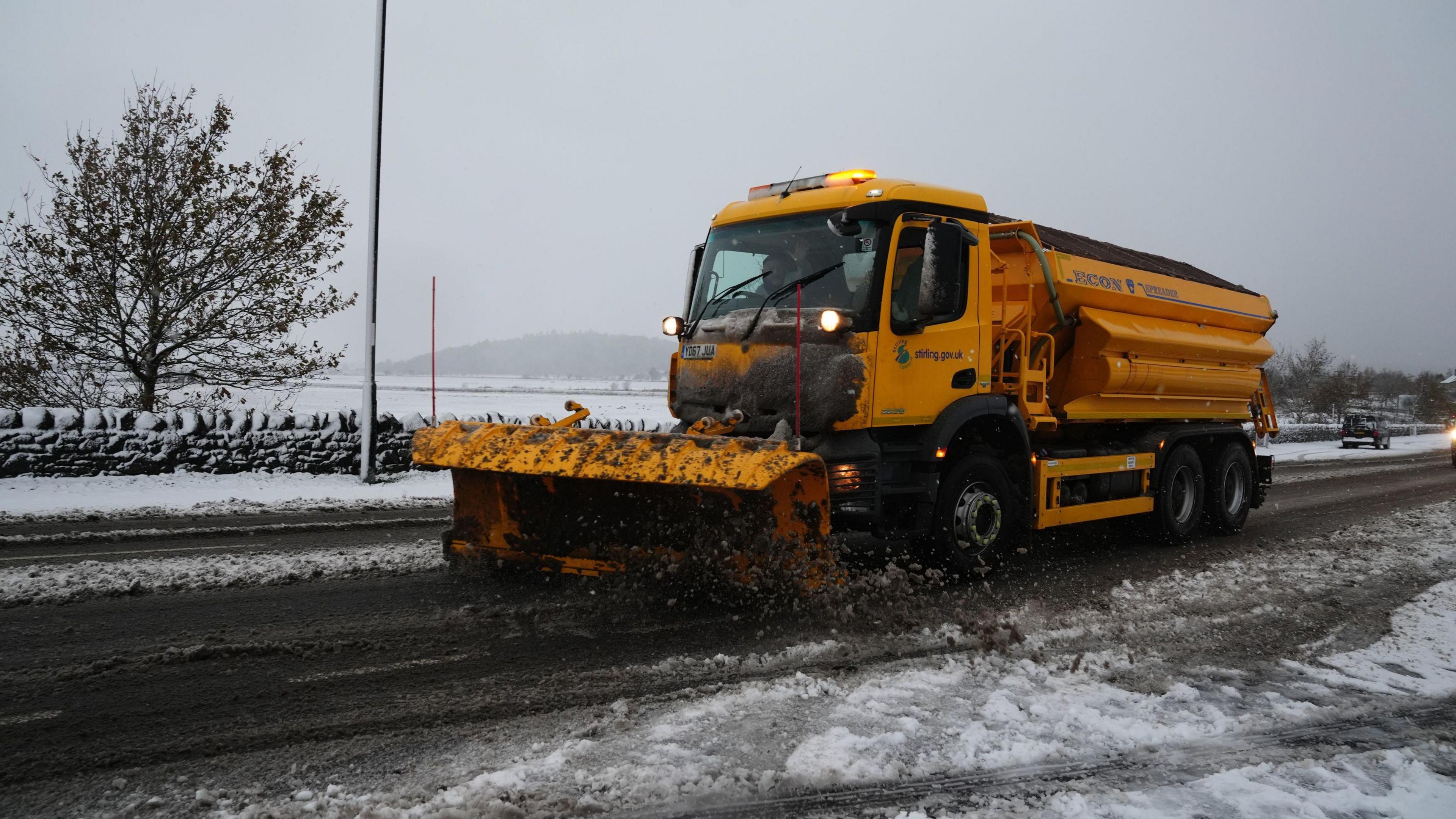 A yellow snowplough clears snow from the road.