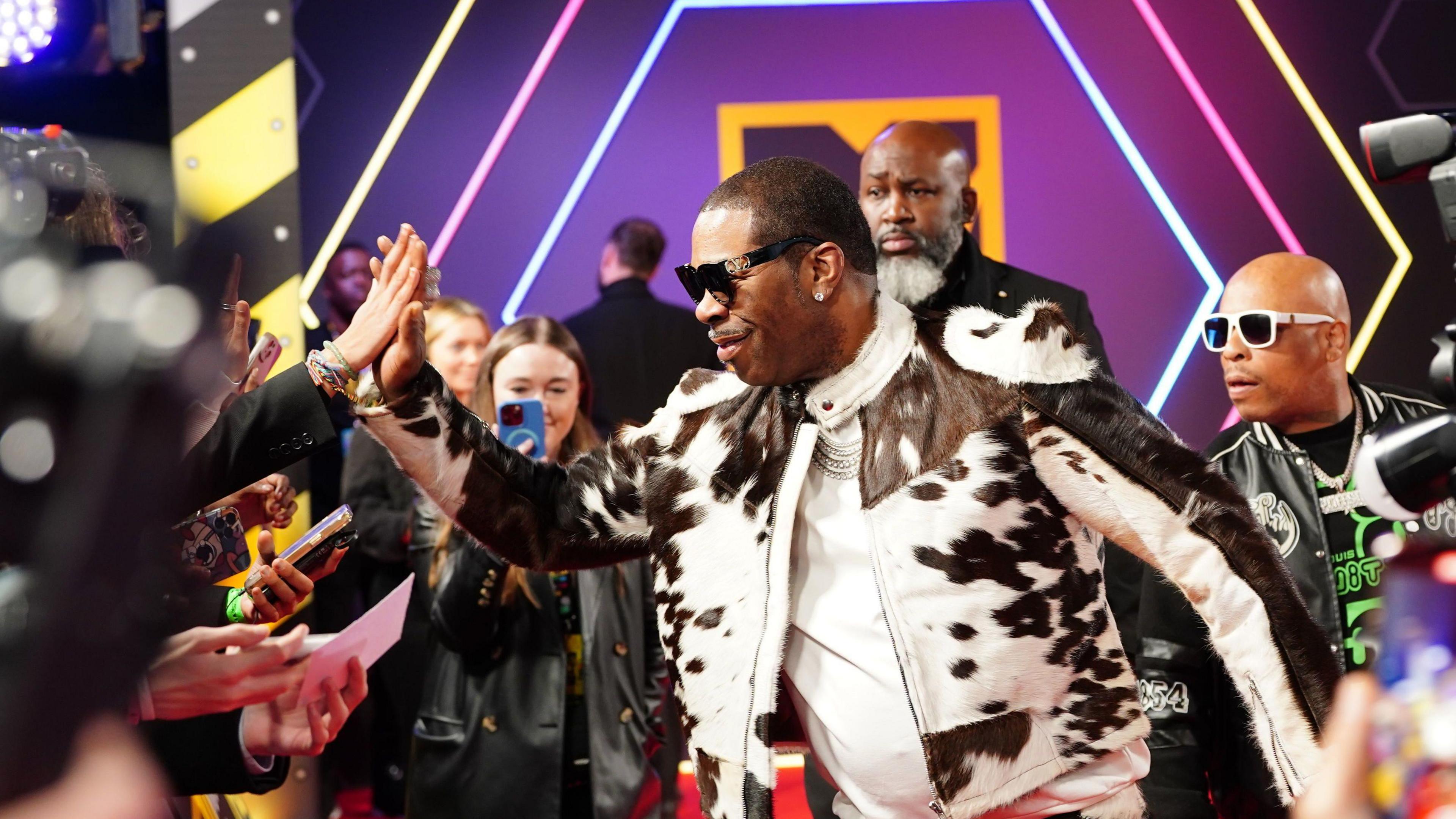 Busta Rhymes in a black and white cowpring leather jacket and high-fiving a fan