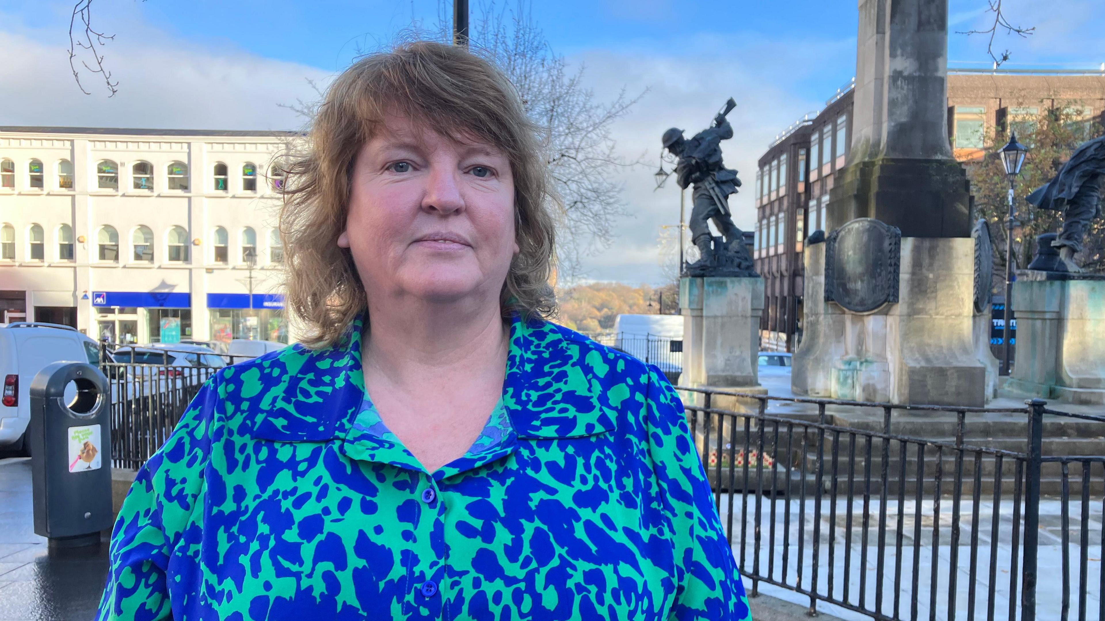 Derry's deputy mayor Niree McMorris , wearing a blue and green dress and with fair hair, stands in front of Derry's war memorial
