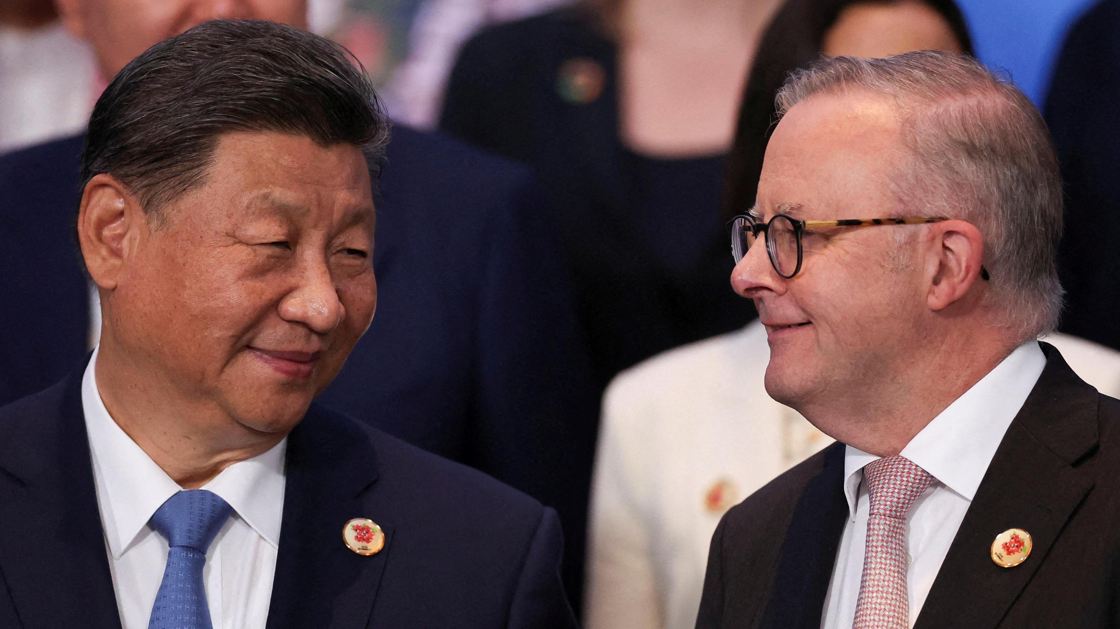 Chinese President Xi Jinping and Australian Prime Minister Anthony Albanese smile at one another in a close up, both wearing suits.