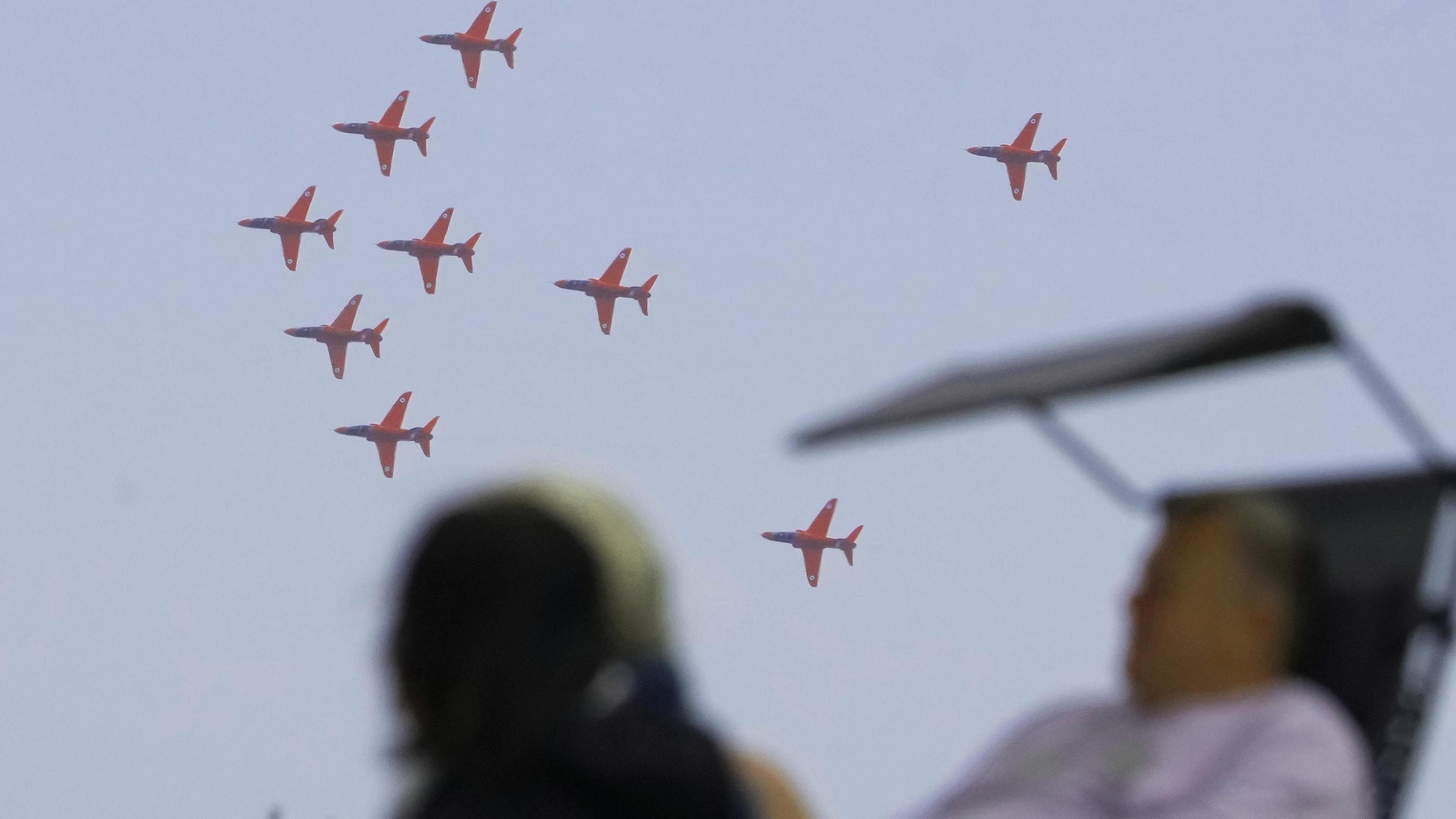 People watch a formation of planes flying in the sky. 