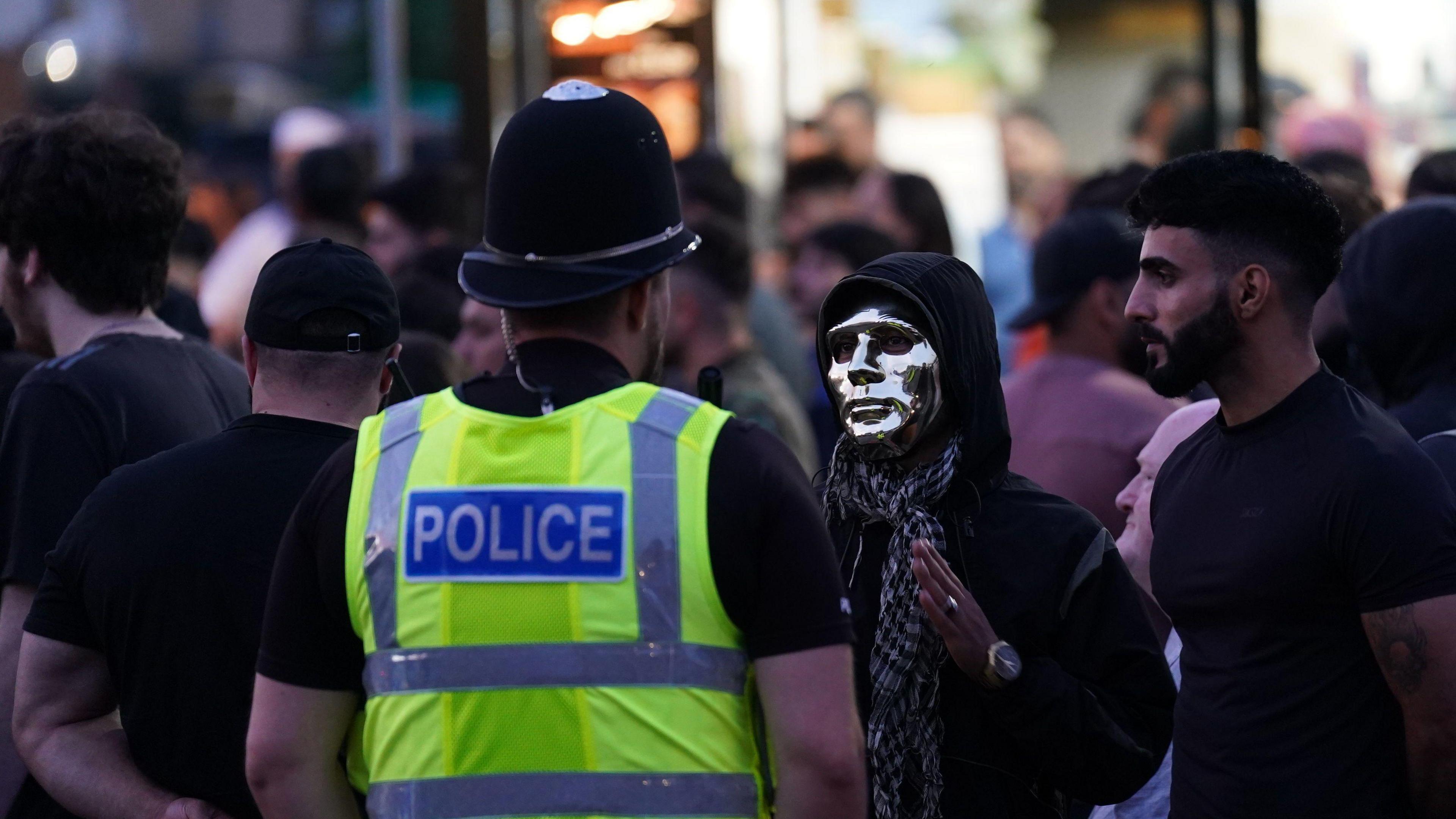 A person in a silver mask talks to a police officer during a demonstration