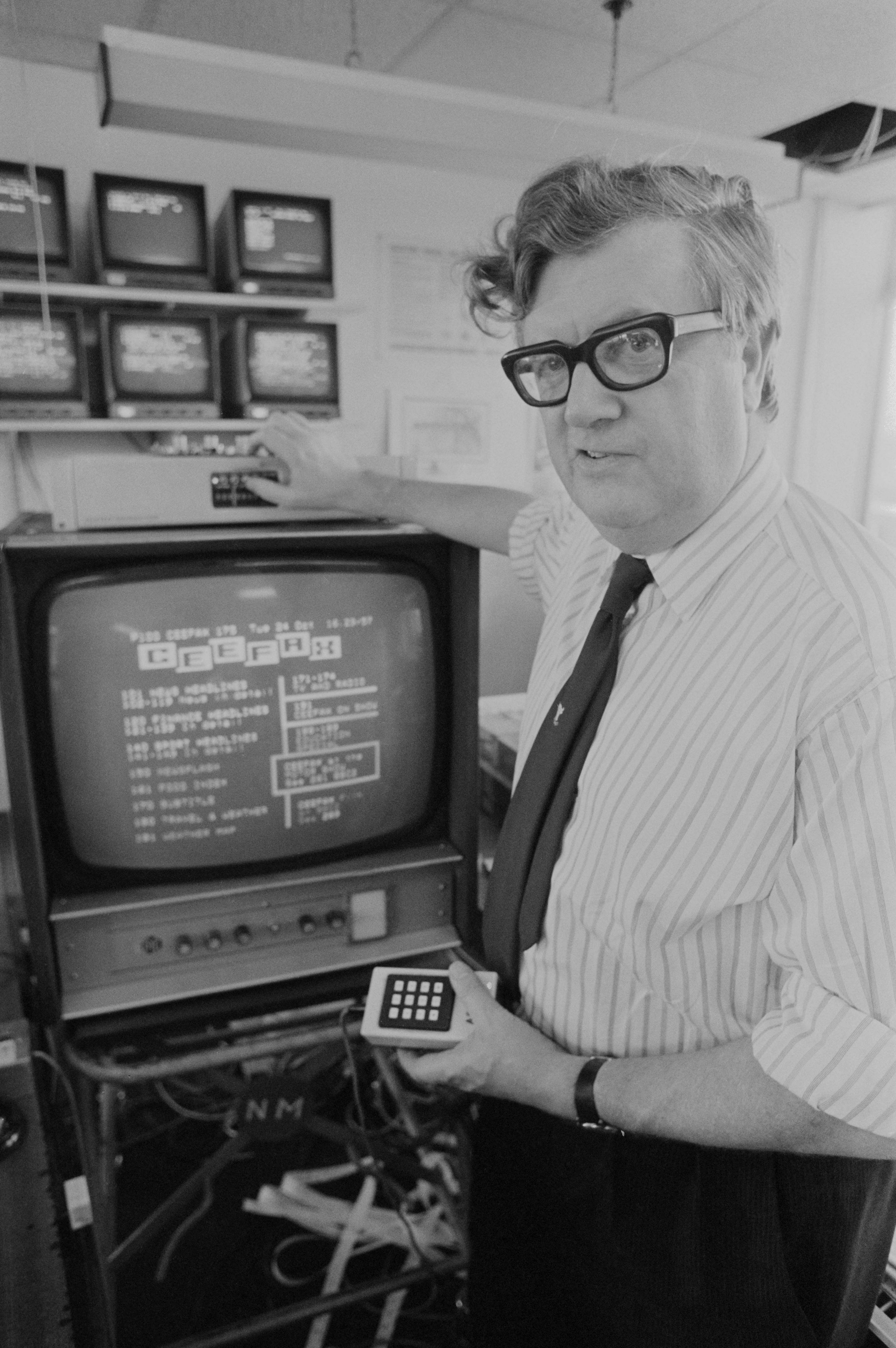 Journalist, Colin McIntyre, pictured holding a remote control with a television set showing Ceefax.