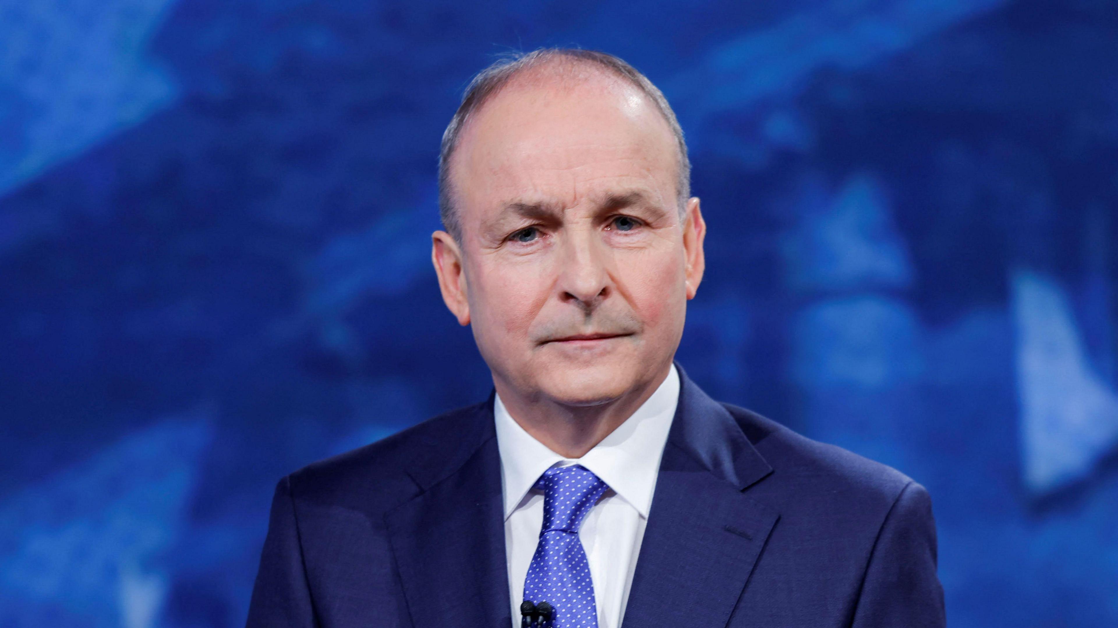 Micheál Martin looks on on the day of the final leaders' debate ahead of a general election, in Dublin. He is wearing a dark blue blazer, white shirt and blue polka dot tie.