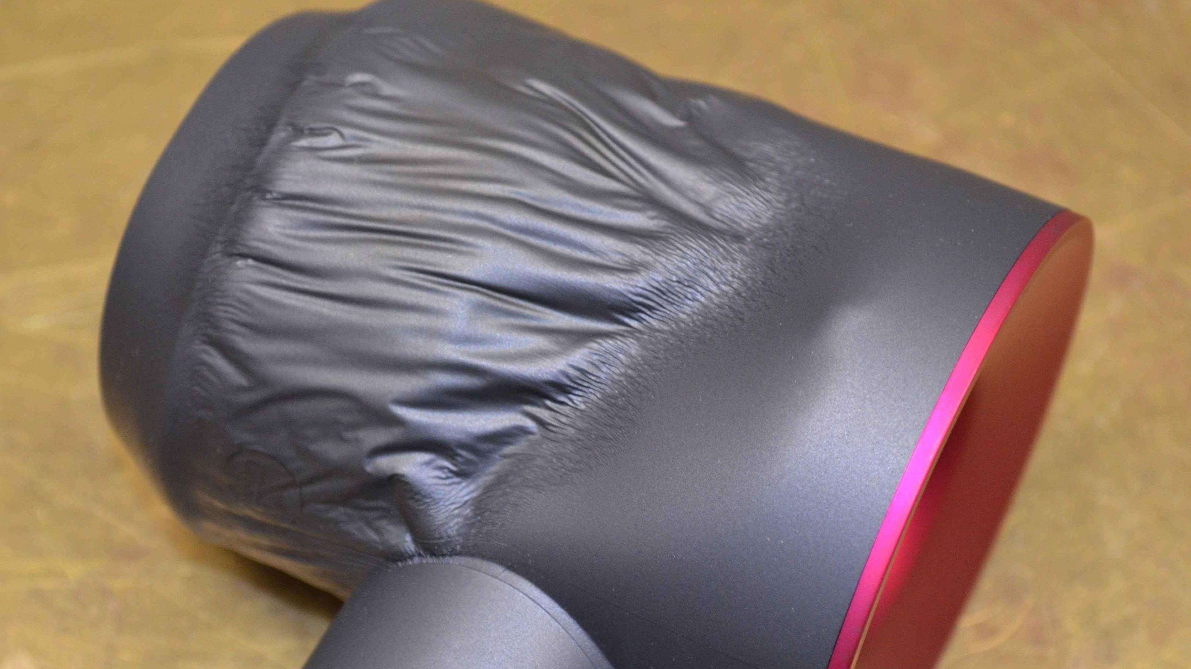 A grey coloured hair dryer with a pink bottom has a large melted part on its exterior.