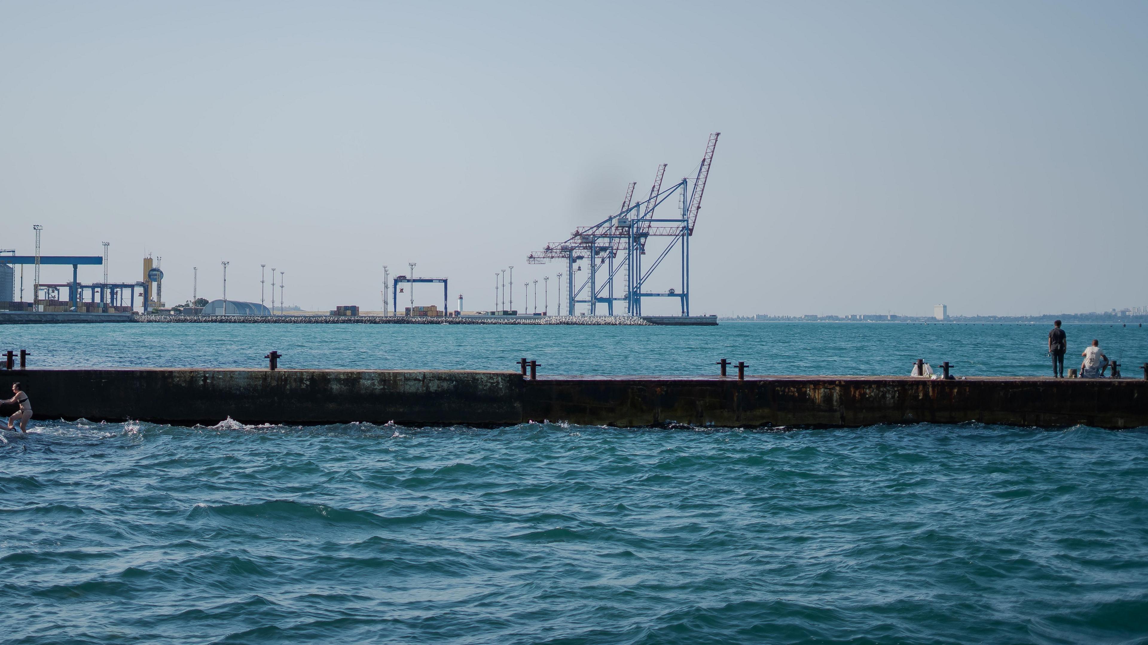 A man on a pier looks at a line of cranes in the distance at Odesa's port. There is not a single ship in the shot, showing how empty the docks are amid recent Russian attacks