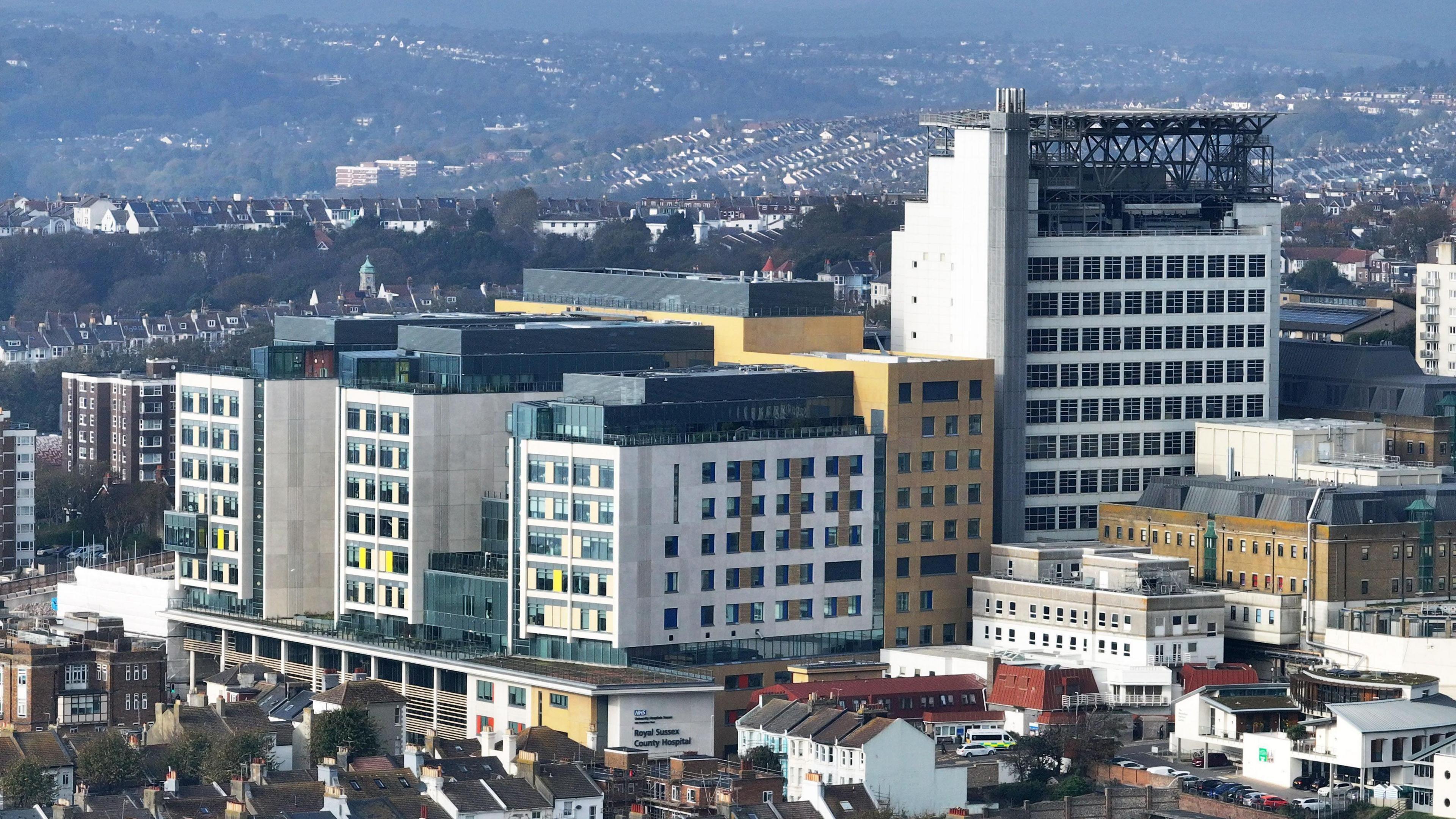 An aerial photograph of a building made of three multi-coloured arms with a tower to the right of it.