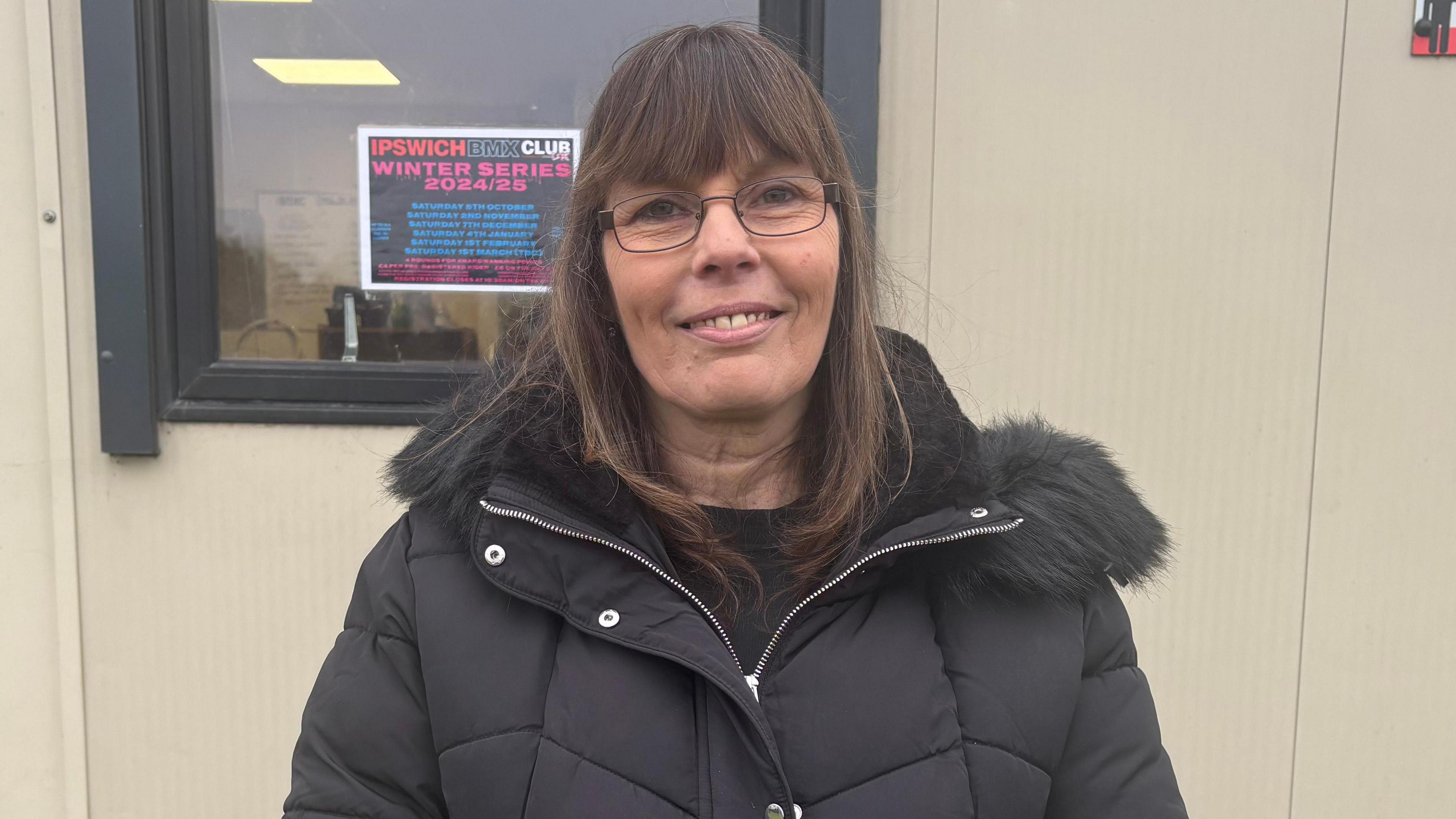 Tracey Reeve, wearing a black coat stand in front of the clubhouse.