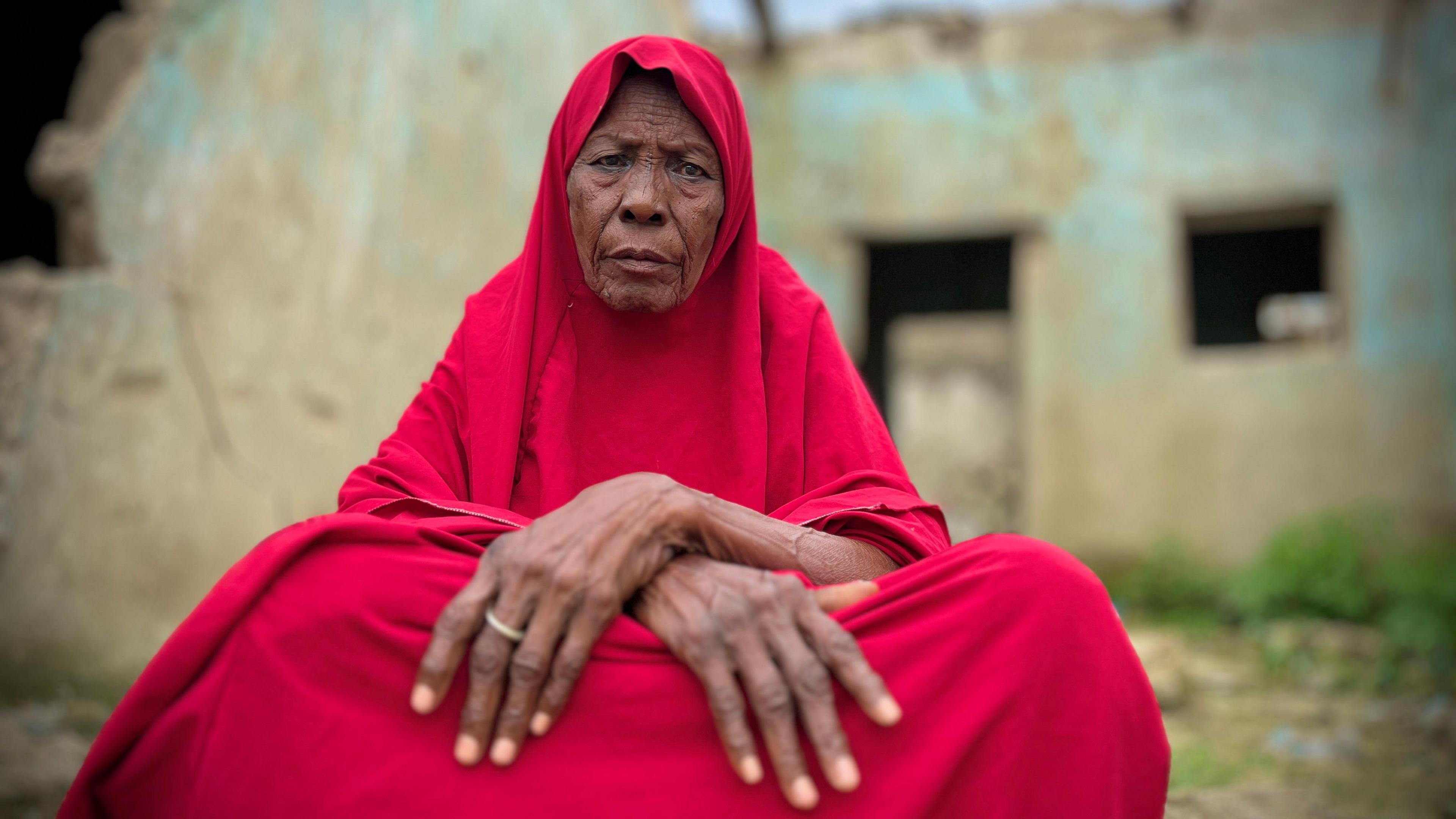 Maryam Jidda sits as she wears a red jilbab and stares into the camera