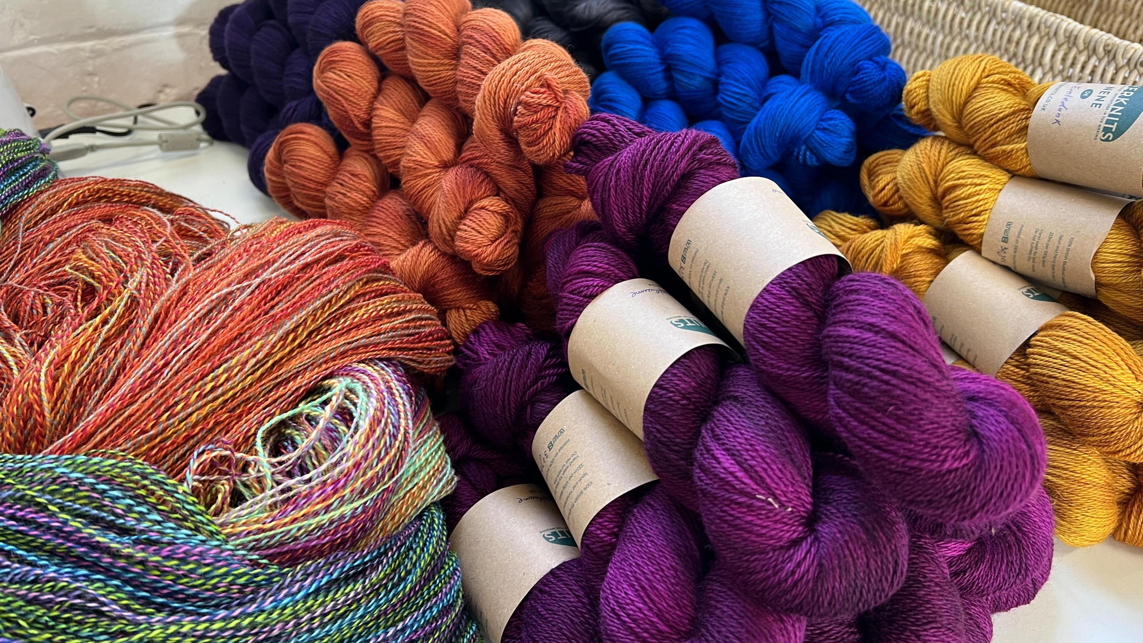 Colourful bundles of yarn, including purple, fiery orange and blue, that has been hand dyed in Becci and Marcus's workshop