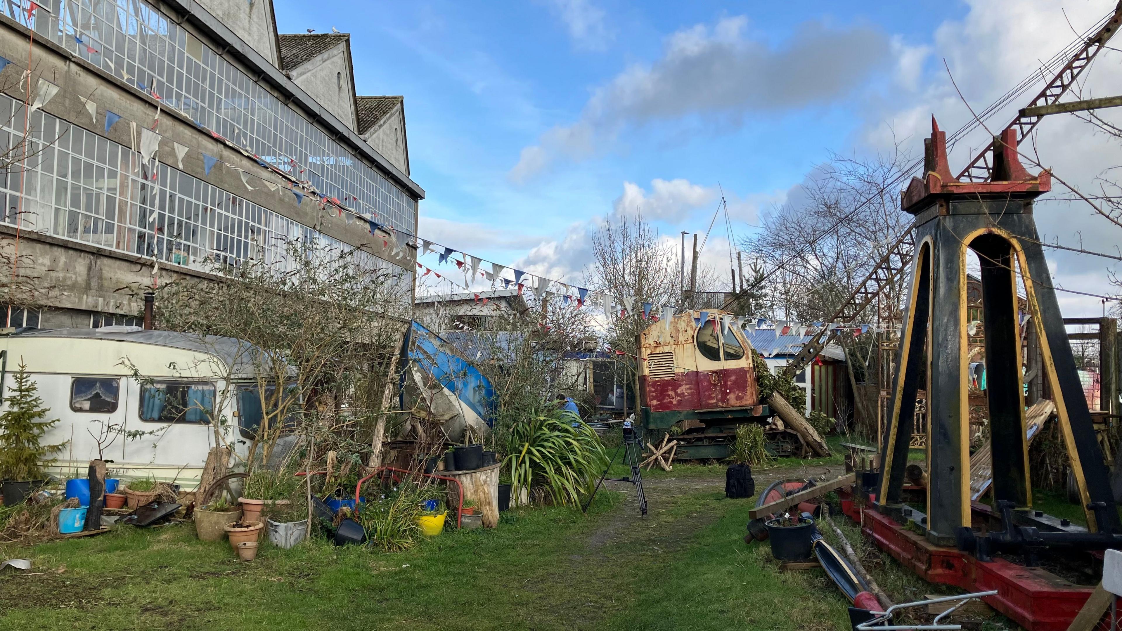 The ground of the Zig Zag building. In shot is part of the building, a caravan, a crane and an historic engine.