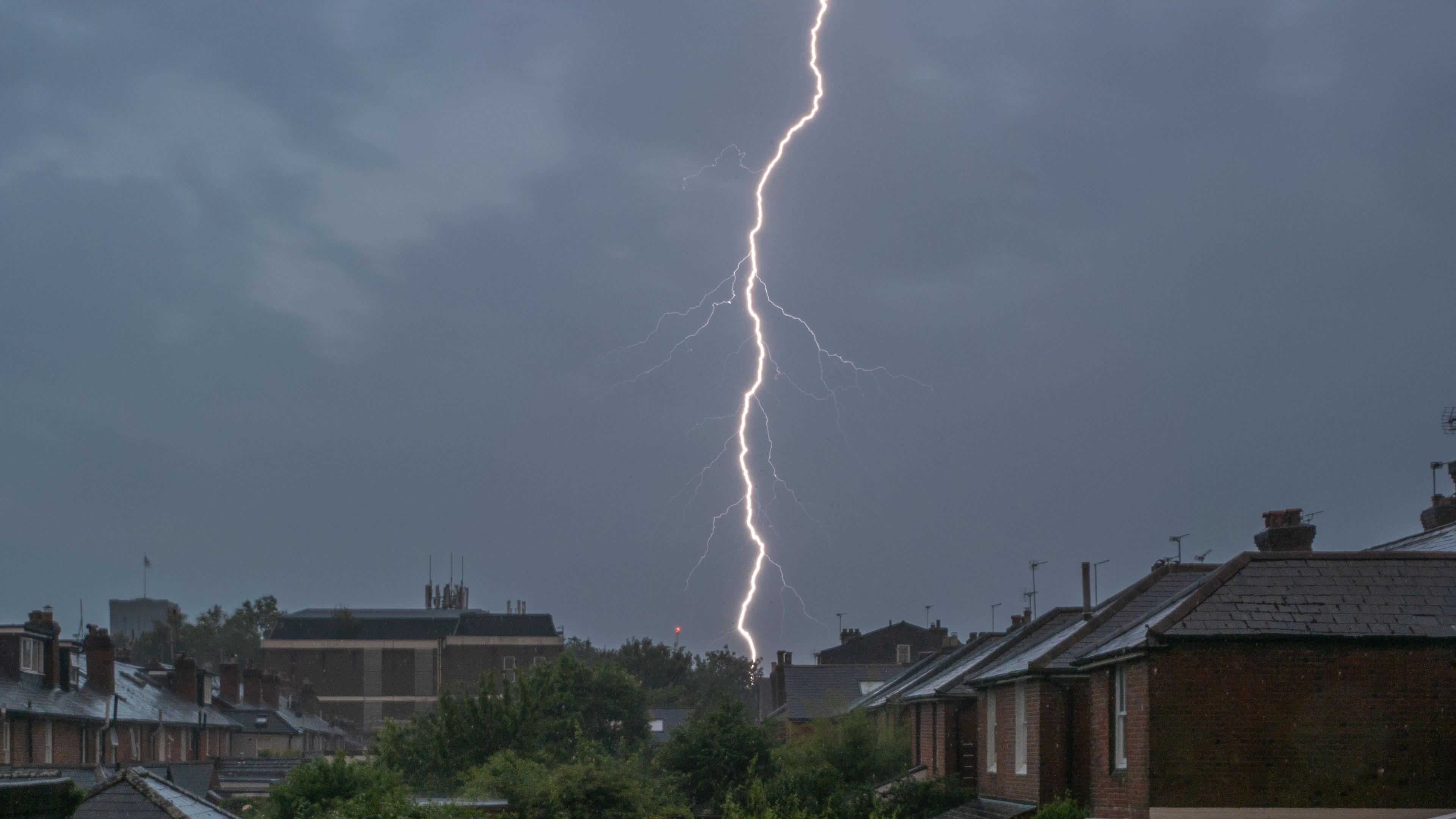 A single strike of lightning against a dark sky over rooftops