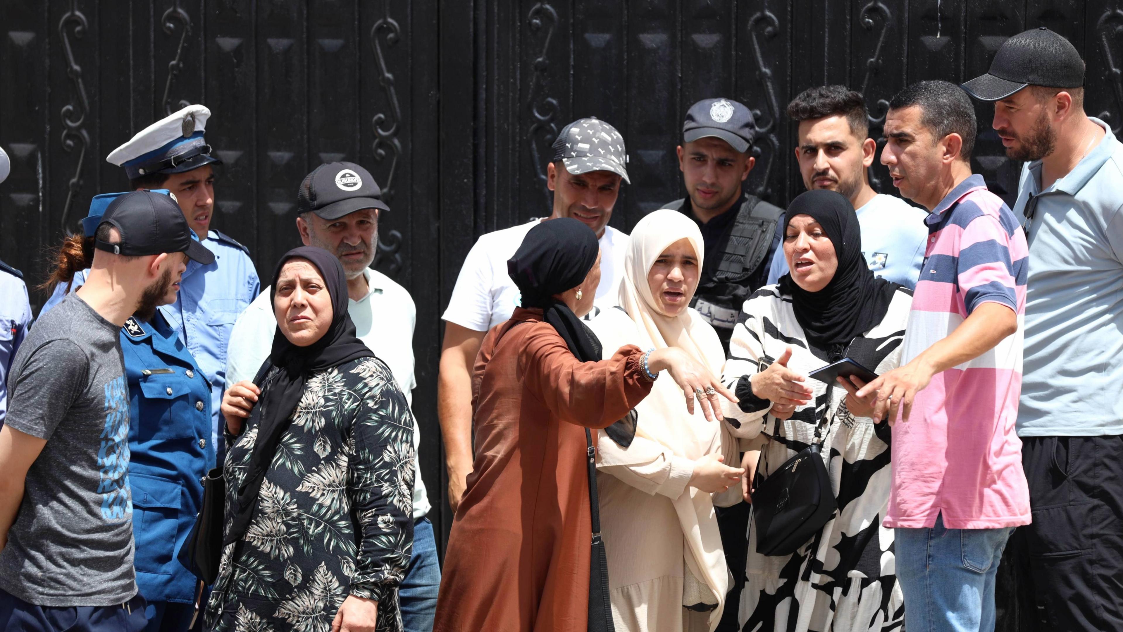 Police stand guard at a black gates of an orphanage in Algiers as a crowd of men and women gesticulate outside