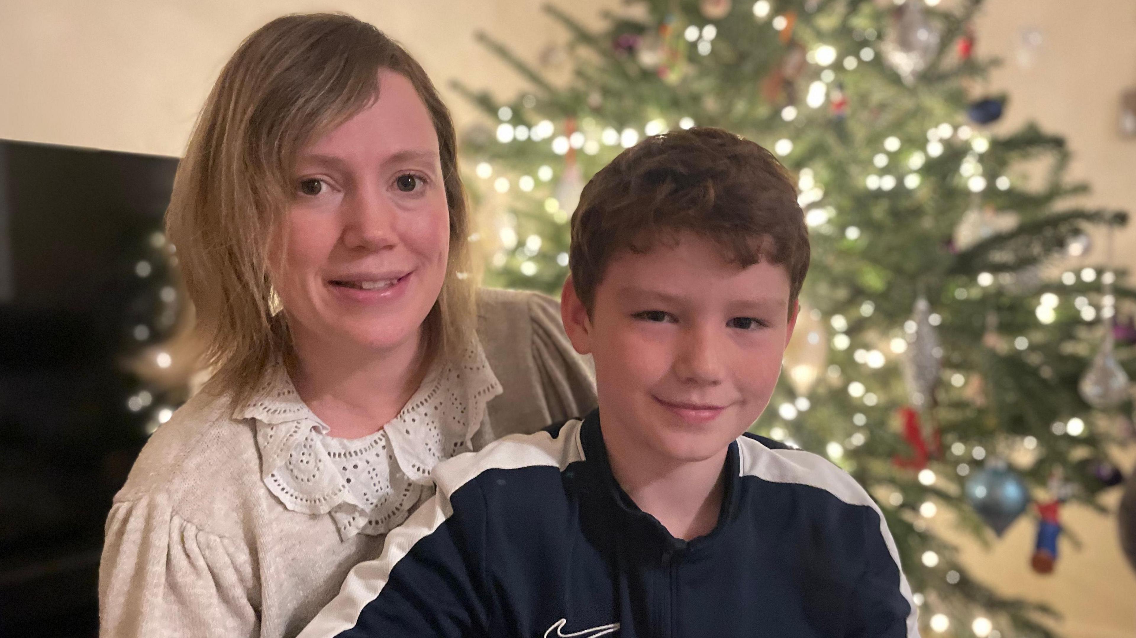 Harry and his mum Sophie sat in front of the Christmas tree at their home. Both are looking into the camera and smiling. Sophie has her arm around her son.