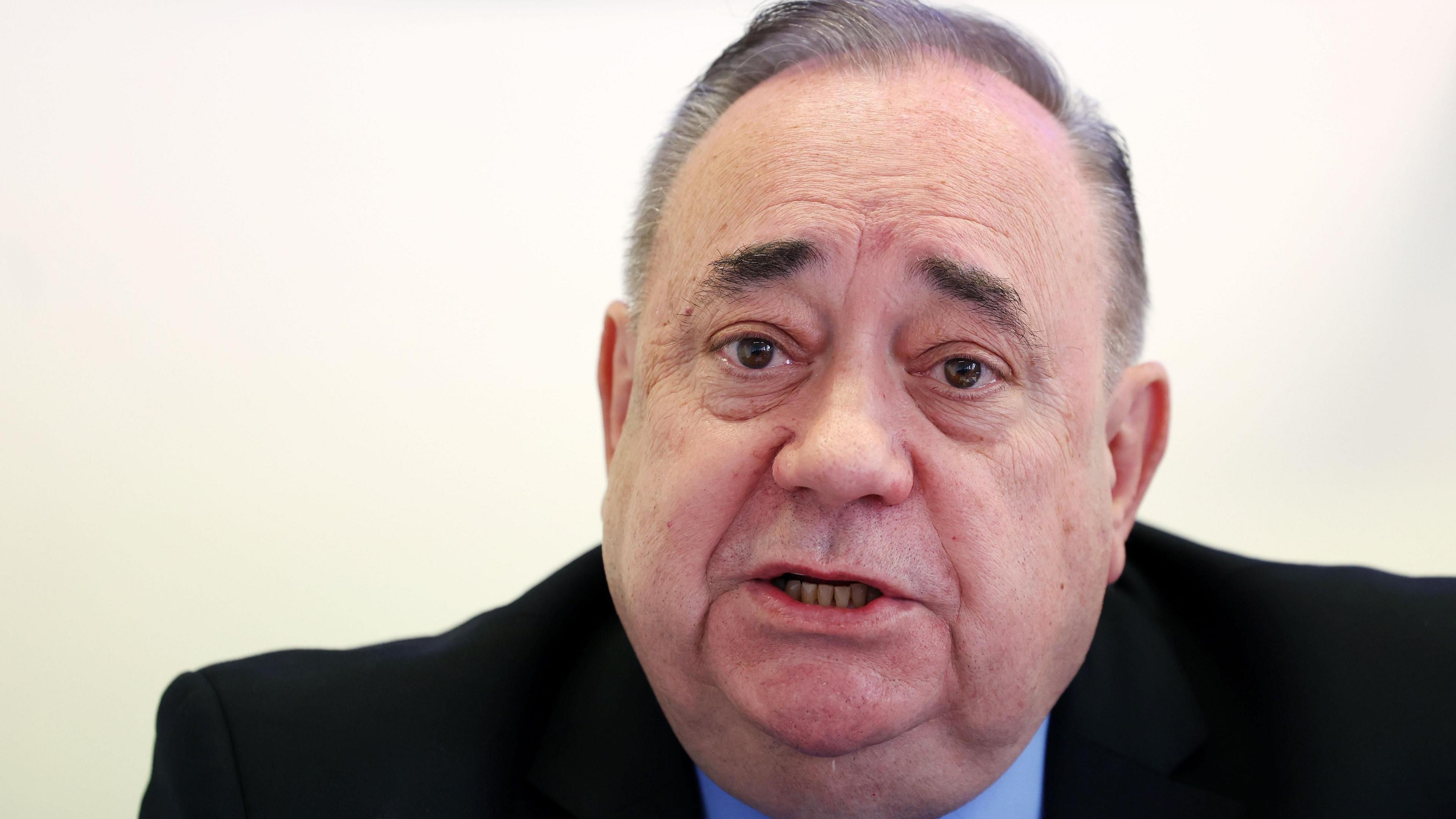 Alex Salmond against a white backdrop. He is speaking and looking off to the side. 