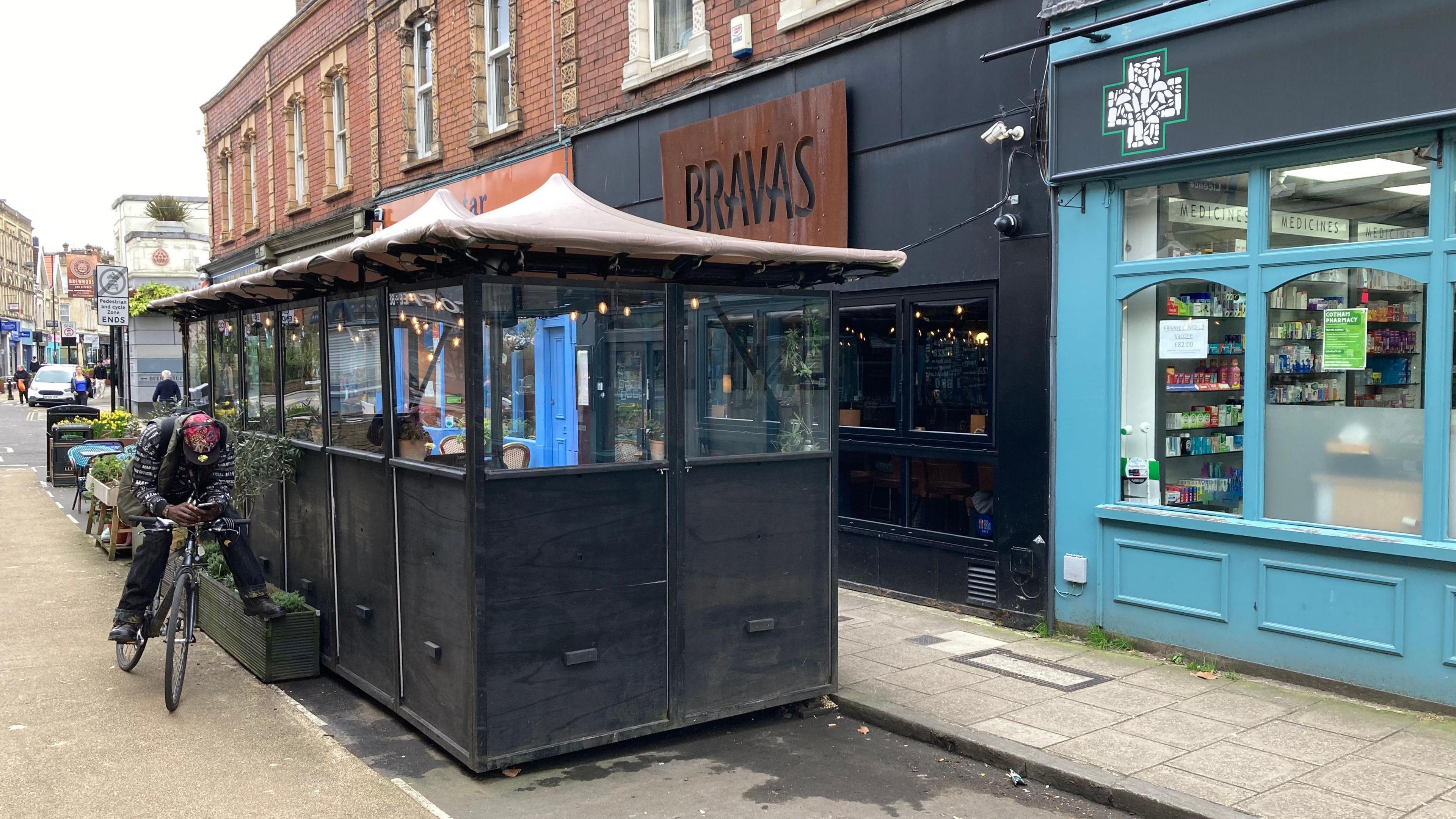 An outdoor seating area with a canvas outside the pavement, and Bravas shop signage visible behind