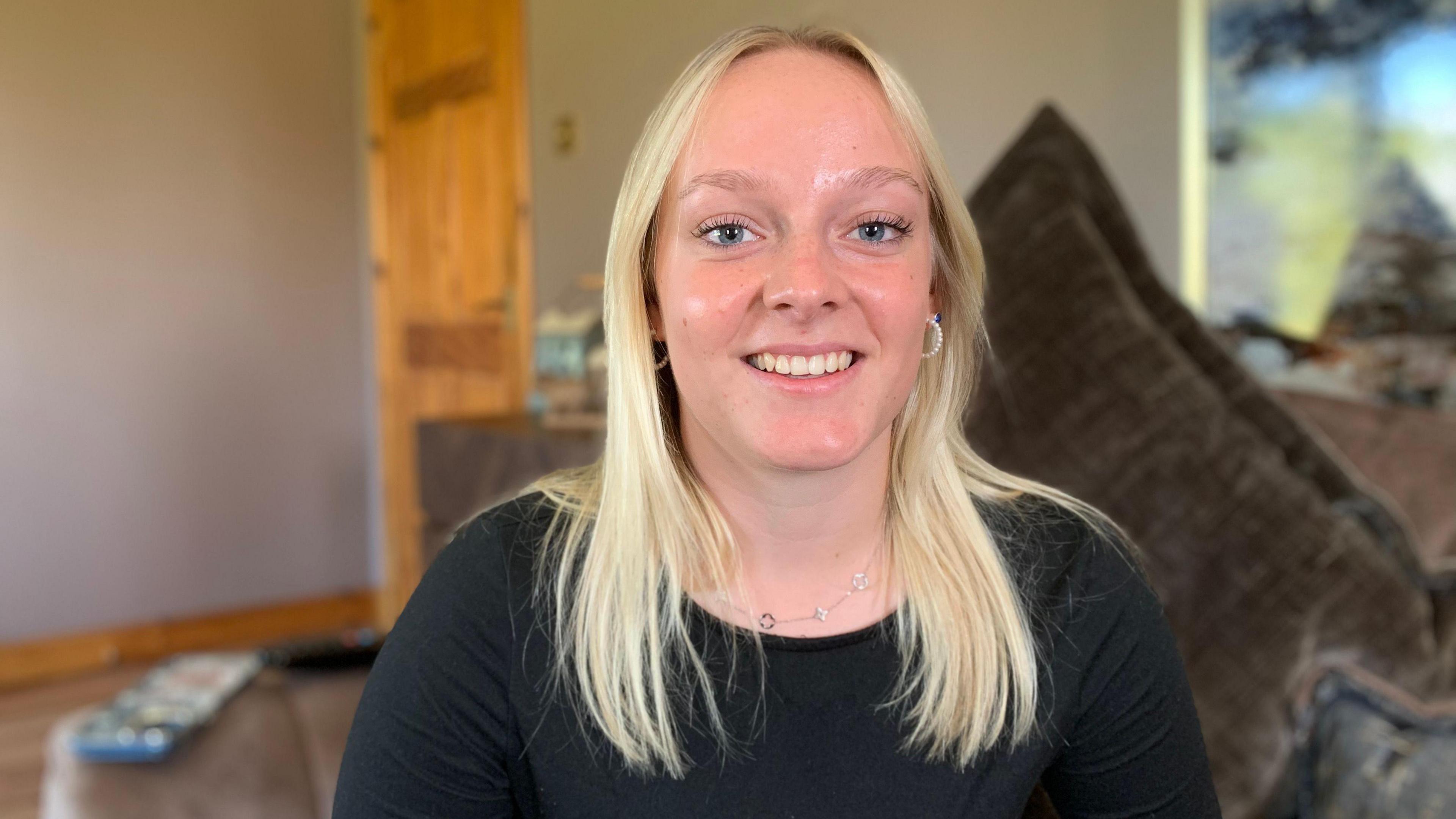 Niamh Muir, who has long, blonde-hair, sits on a sofa. She is wearing a dark-coloured jumper