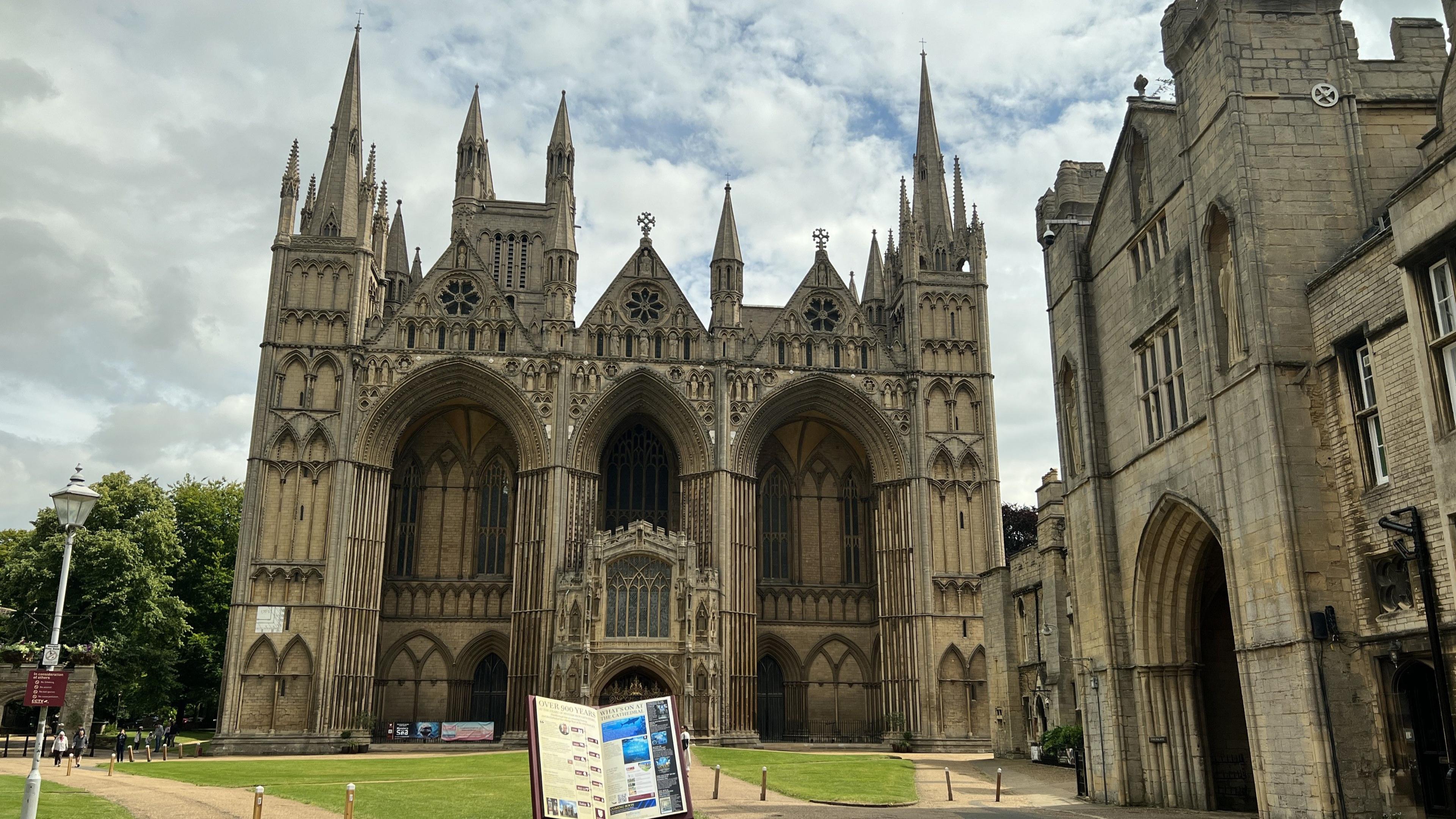 Exterior of Peterborough Cathedral showing Gothic towers and arches and a giant open book at the end of a stone path surrounded by lawns