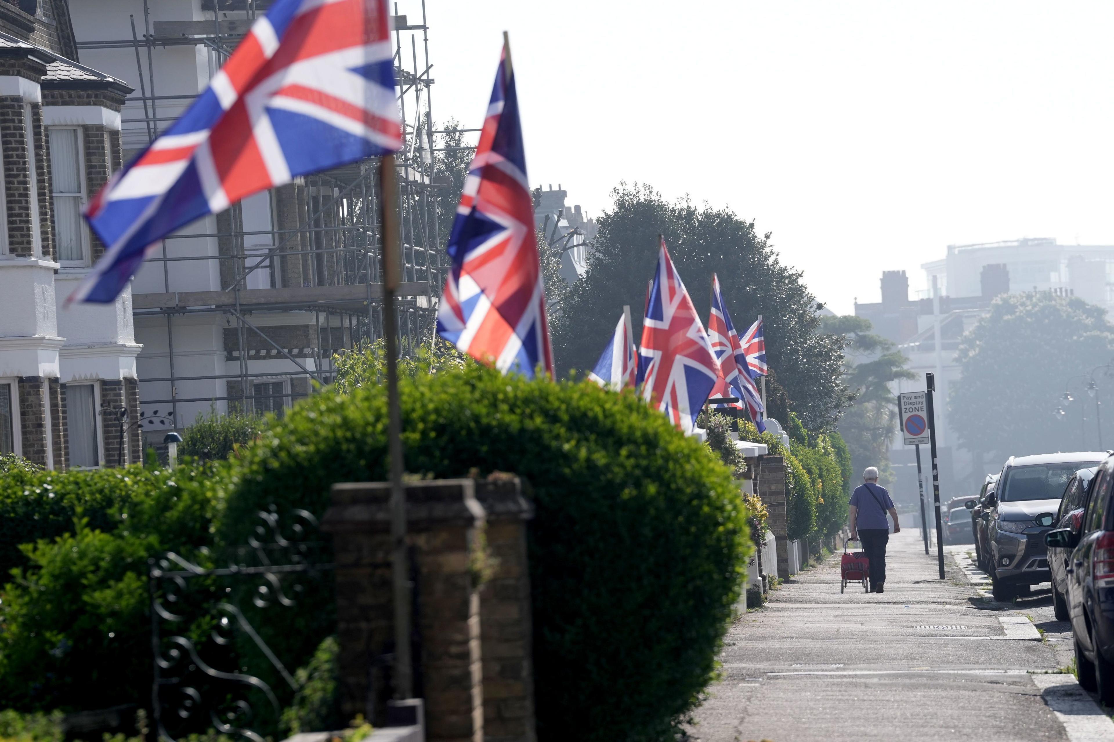 A street in Essex with Union Jack flags and a man with a trolley. There is some high cloud