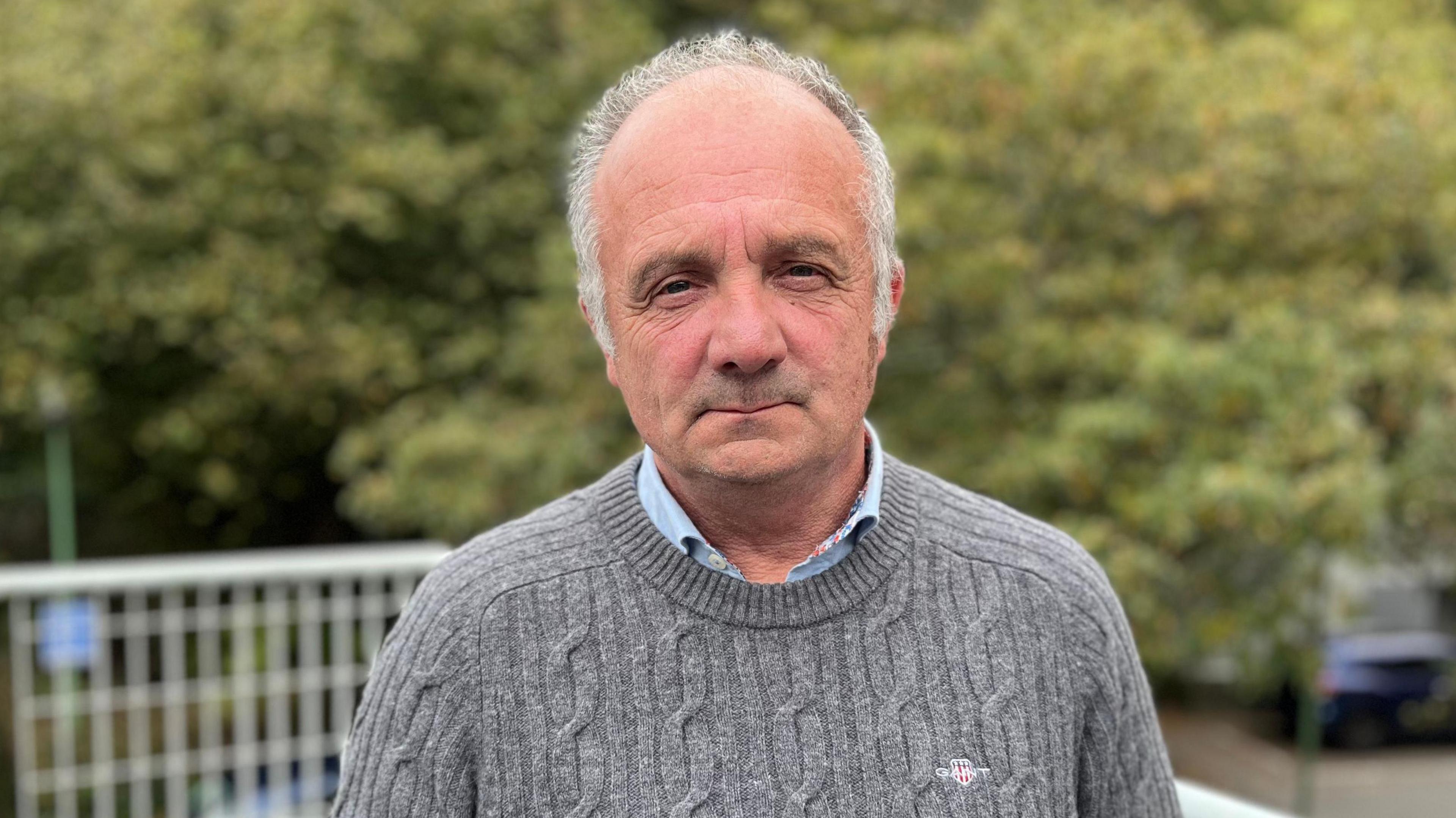 Deputy Neil Inder - A man with thinning grey hair squin ting at the camera. He's wearing a grey jumper with a blue shirt underneath.