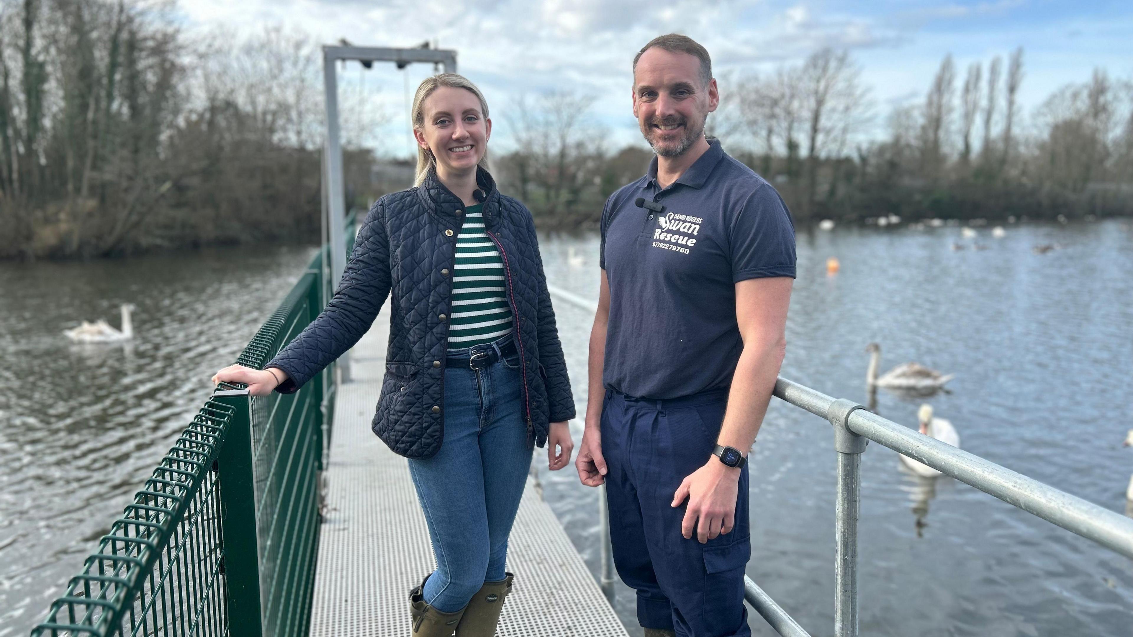 Ellie Vesey-Thompson and Danni Rogers at Shepperton Swan Sanctuary. They are standing on a jetty on a reservoir, both wearing blue outdoor summer clothing.