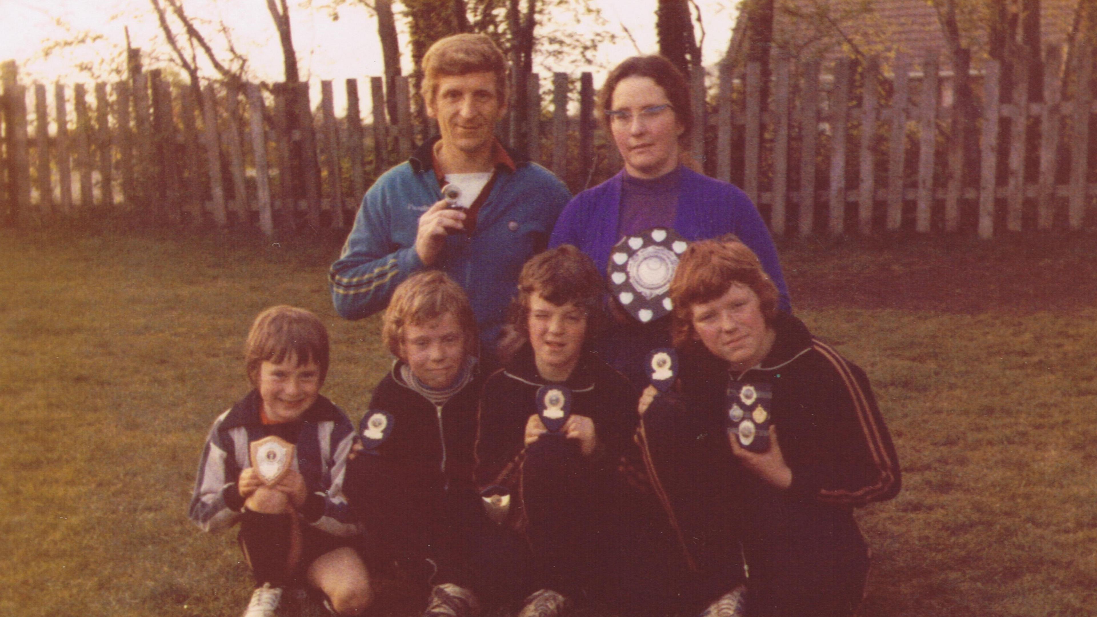 Image taken in the 1970s showing a family of six - Mr Parker and his wife at the back and four boys at the front - all holding little football trophies