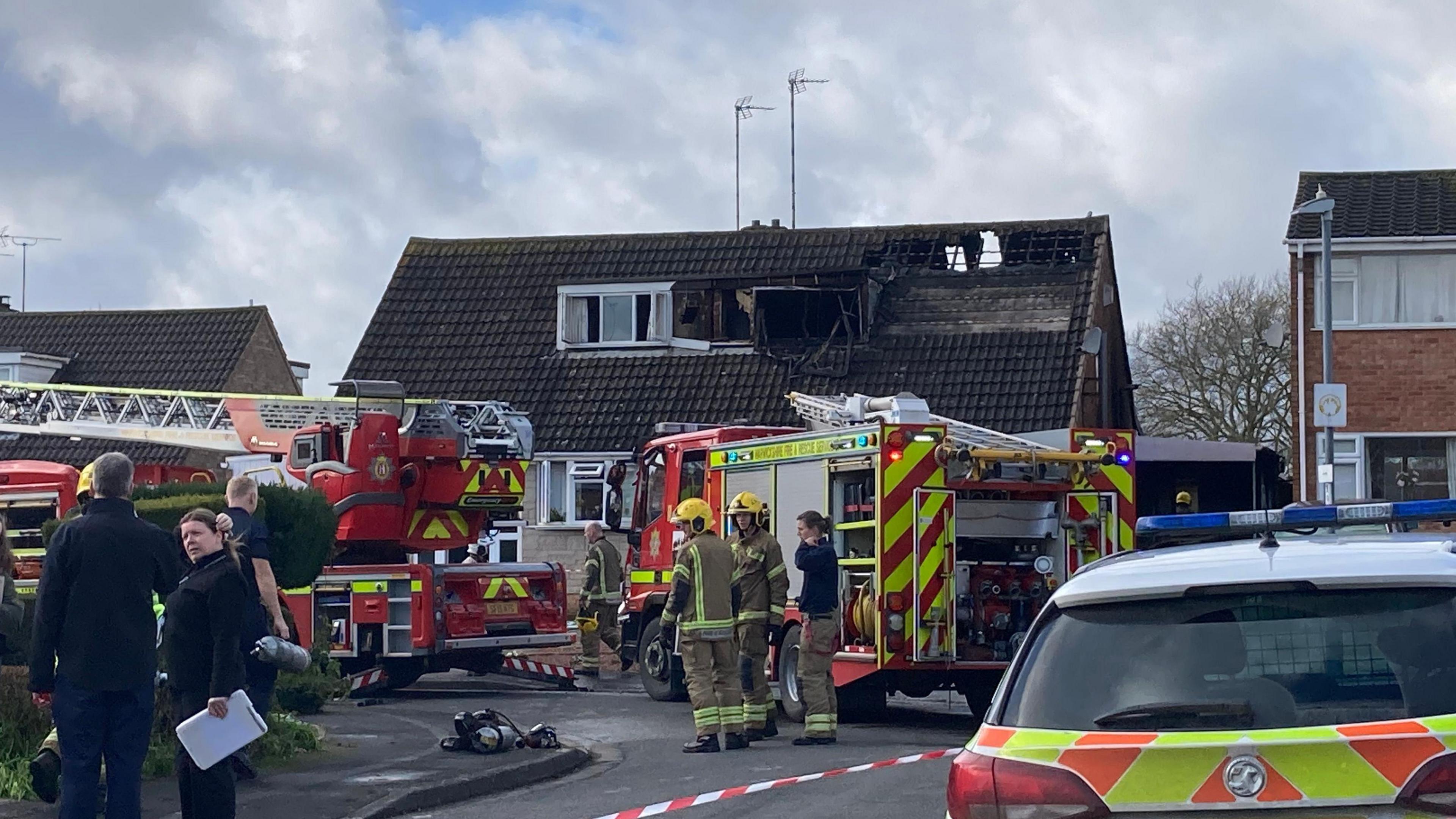 Two fire engines lined up in front of a house with fire damage on the roof.