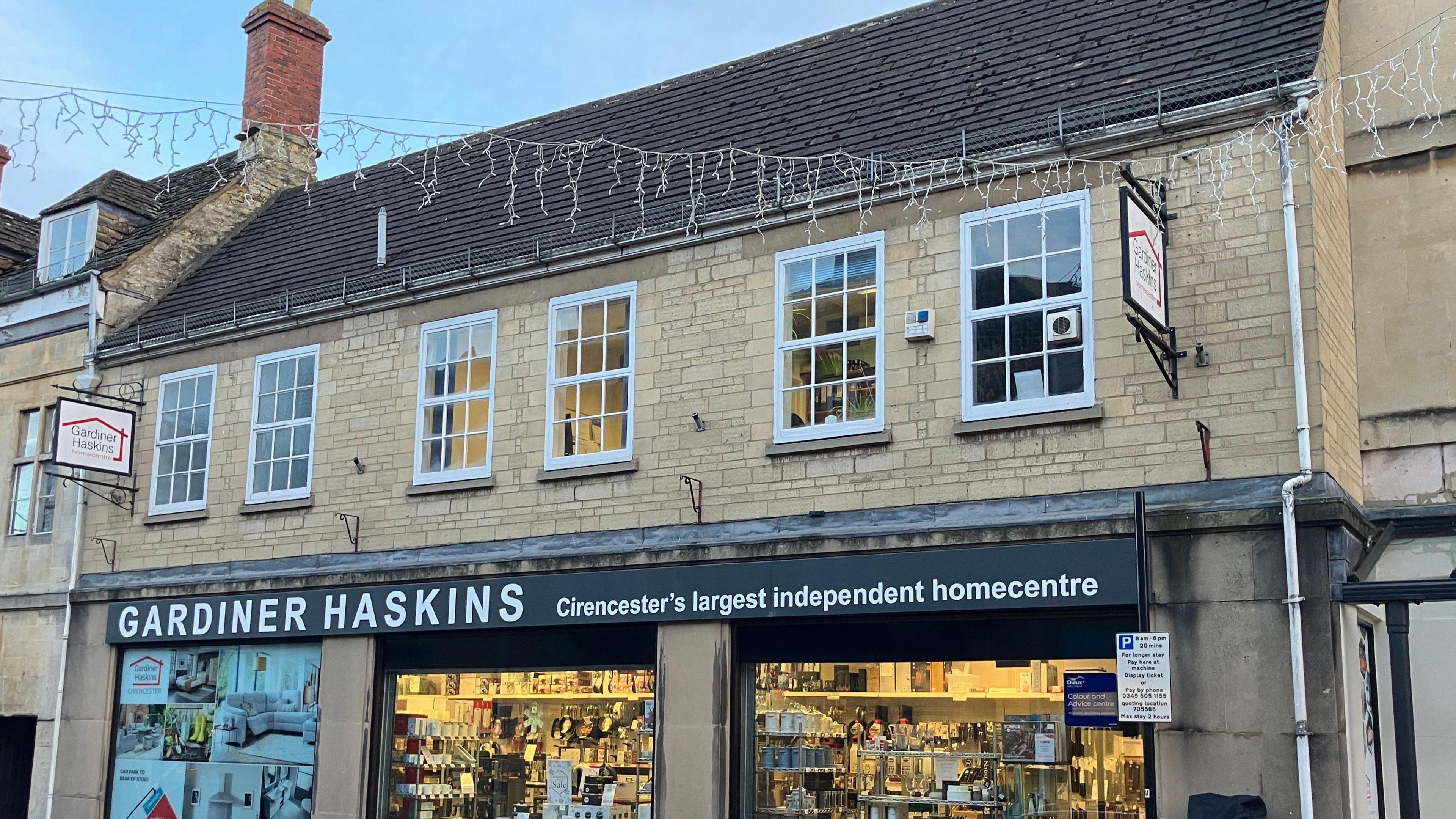 Gardiner Haskins in Cirencester, Gloucestershire. The building is made from Cotswold stone and it has a black store front with white text. 