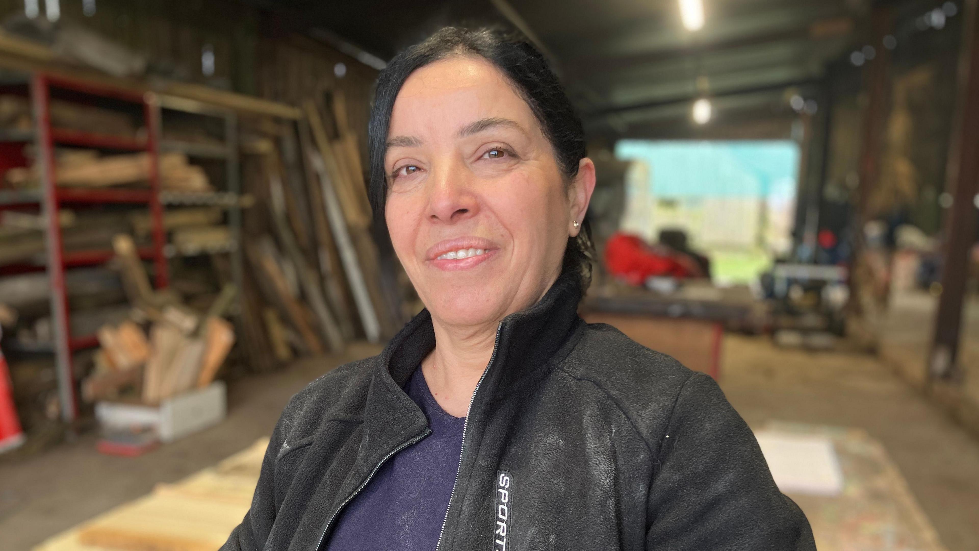 Shiren Abdullah is smiling at the camera. She is wearing a black fleece which is dusted with flour on top of a purple jumper. Shiren has dark hair tied in a ponytail. 