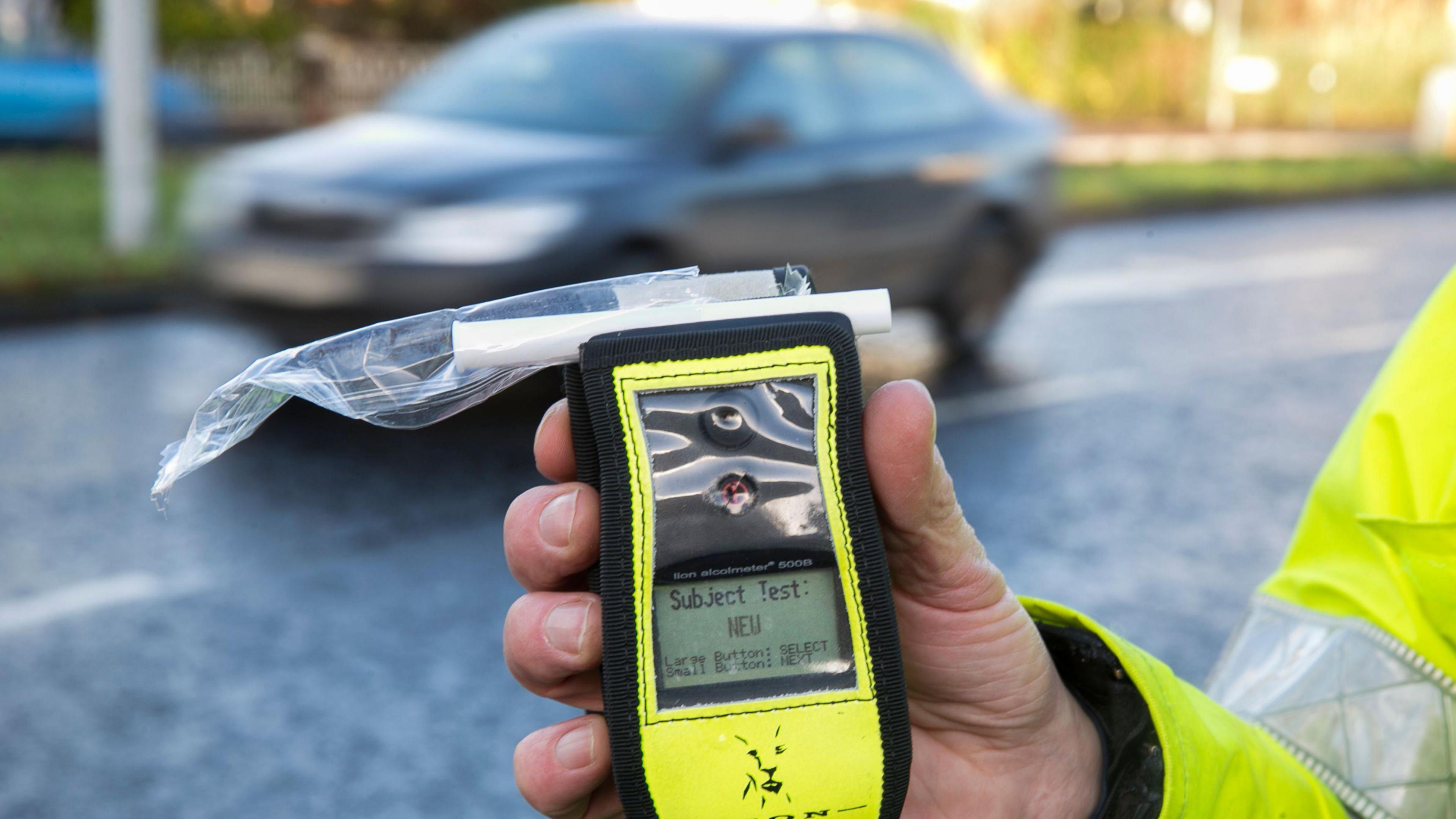 A picture of a breathe test being held in front of a car on a road.