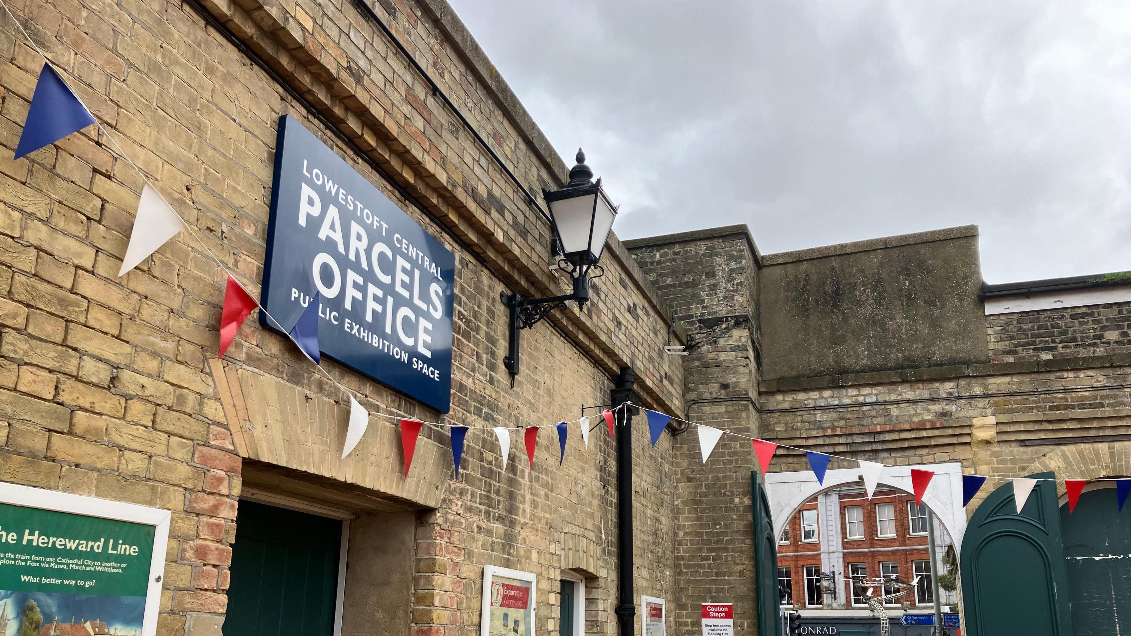 Brick facade showing entrance to the former Parcels Office at the station which is now an exhibition space. Bunting can be seen hanging over a green door.