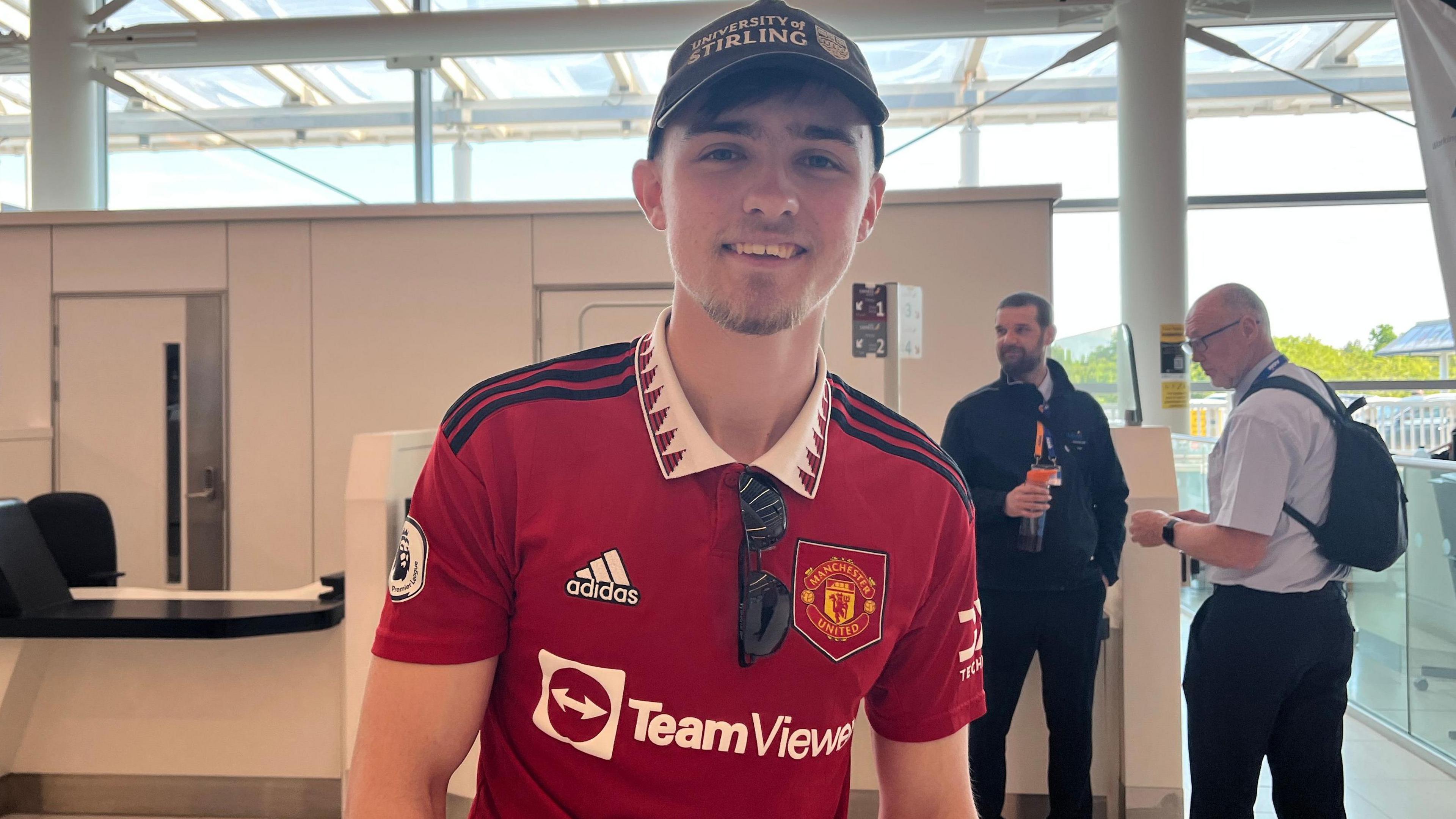 Sam Winton has a current Manchester United shirt and is wearing a blue University of Stirling baseball cap.