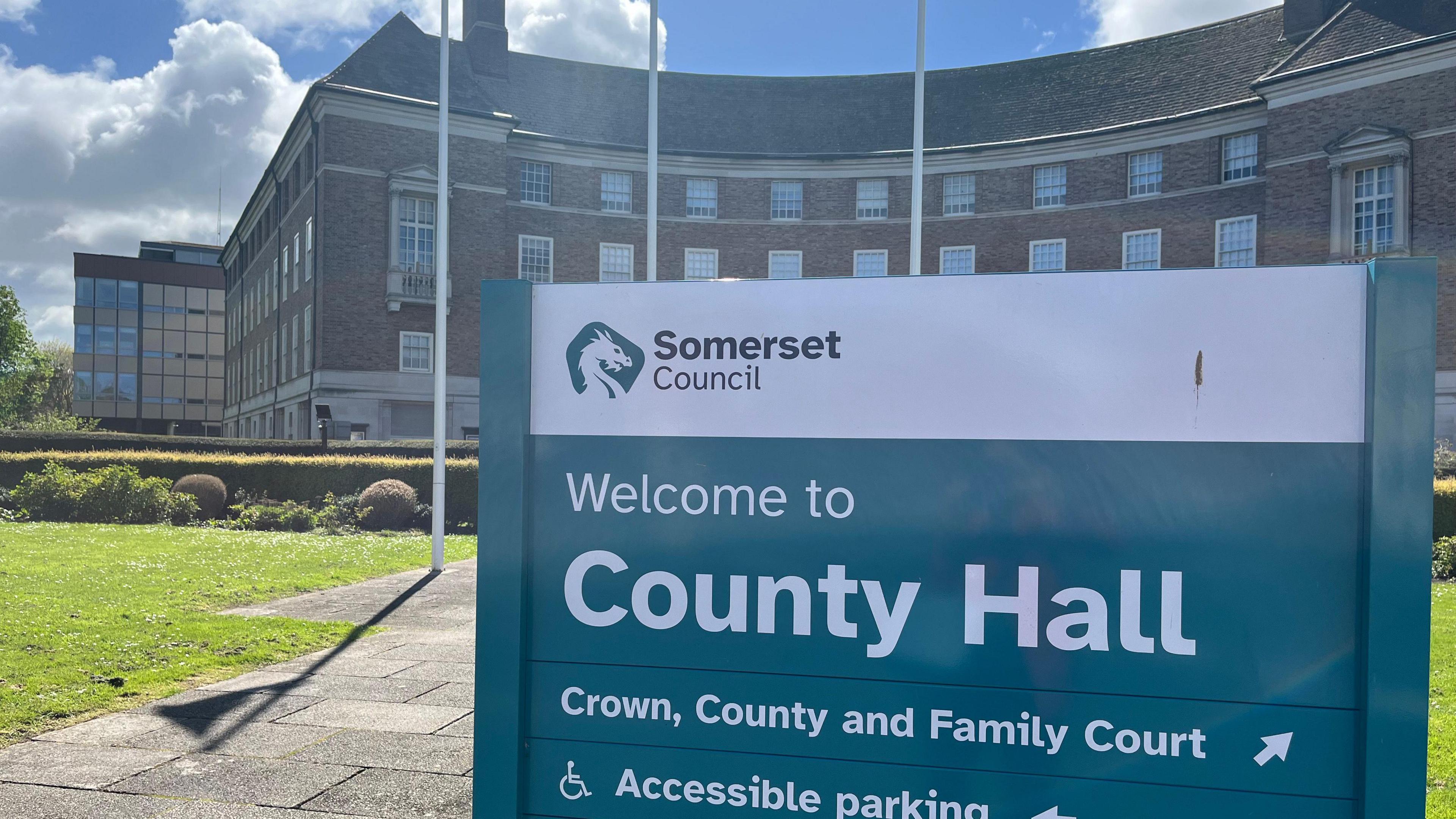 The sign outside Somerset Council's County Hall with the county hall building in the background.