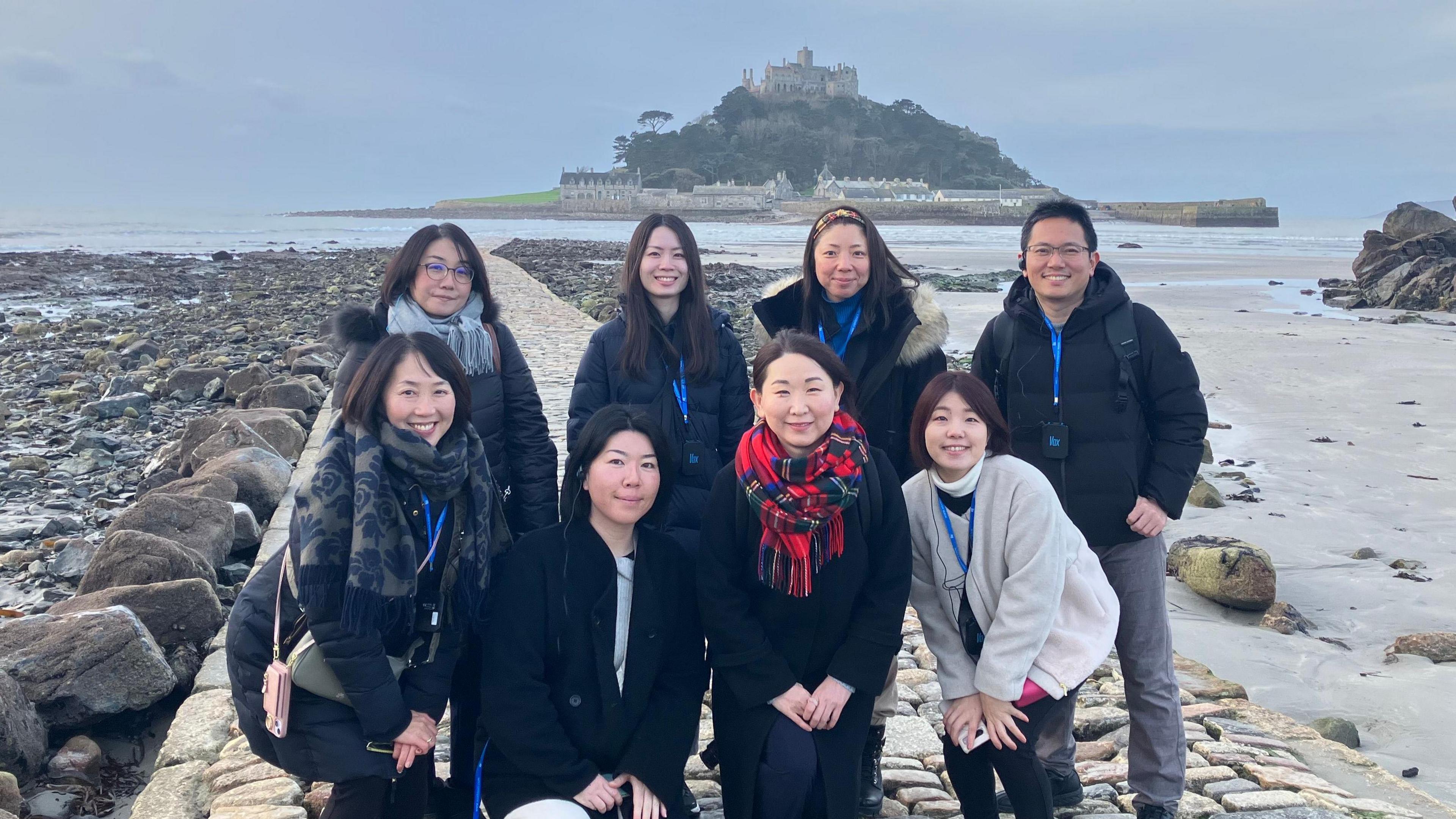 A group of travel agents from Japan are standing in a group in front of St Michael's Mount in Cornwall. 