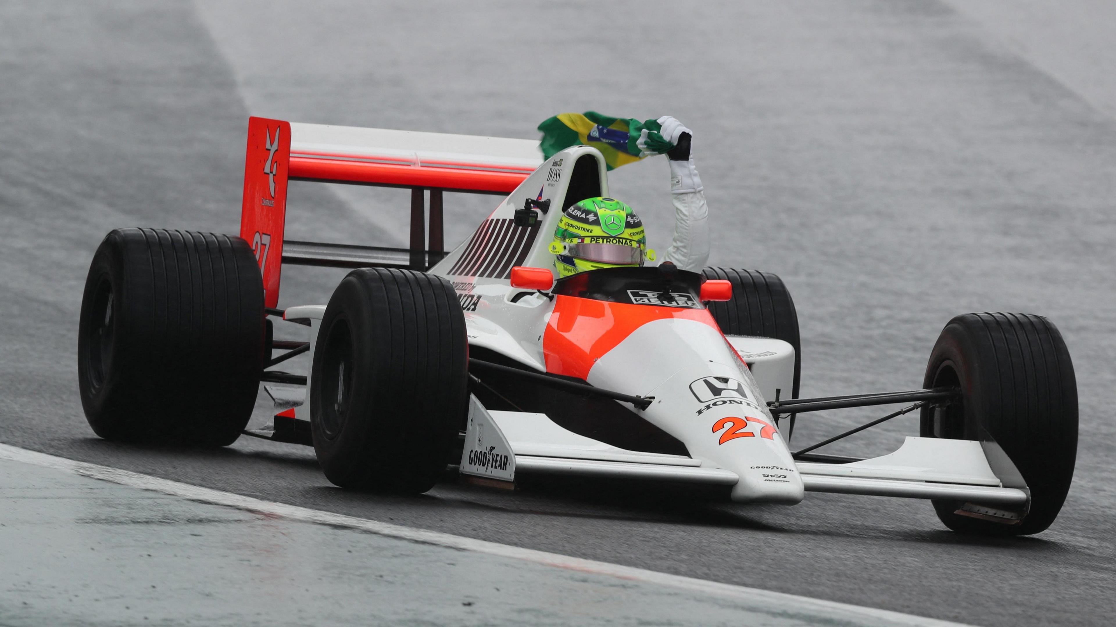 Lewis Hamilton drives Ayrton Senna's 1990 McLaren-Honda at Interlagos,  holding a Brazilian flag above his head with his left hand while doing so