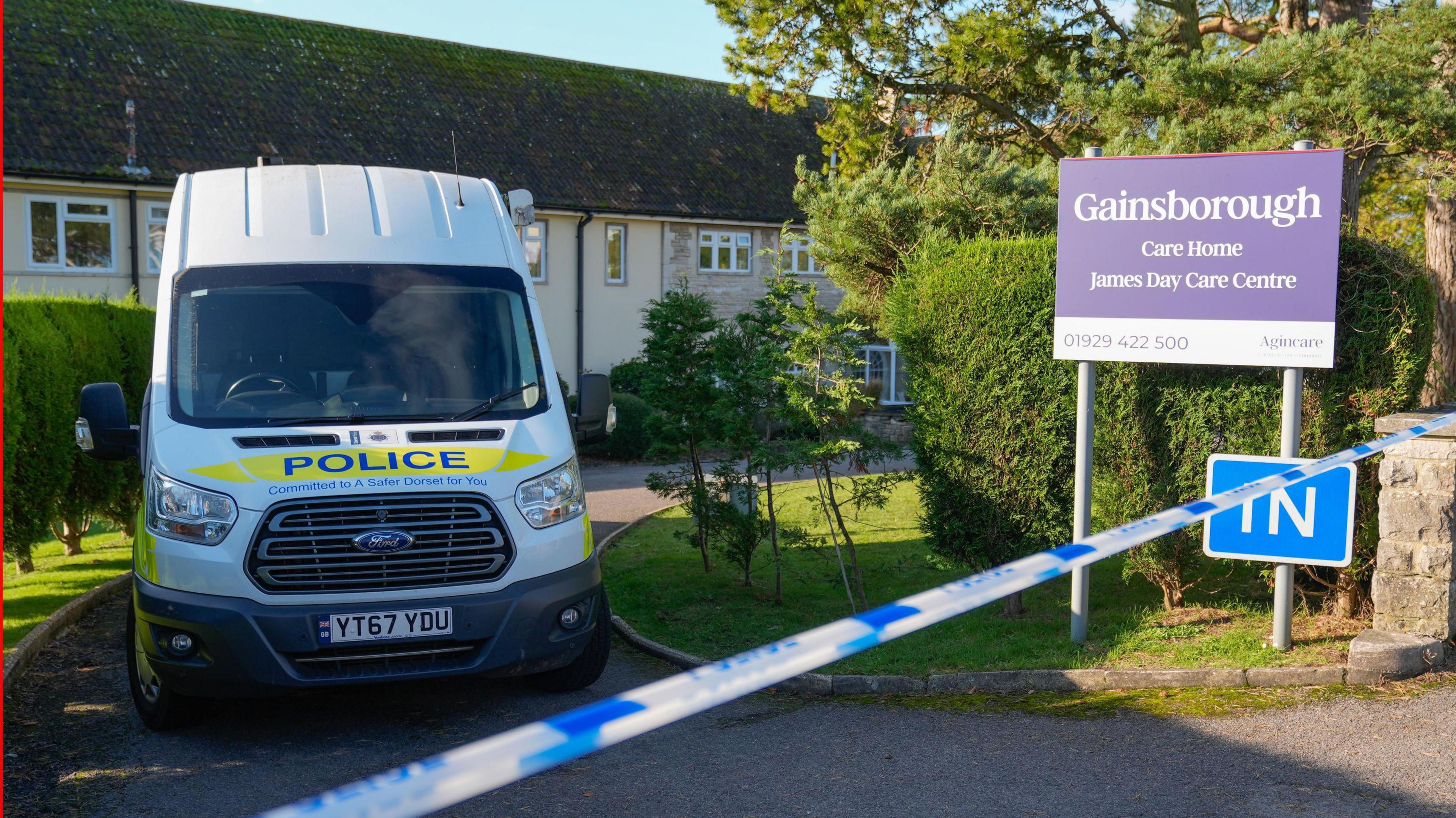 Police tape across the entrance to Gainsborough Care Home. A marked police van is parked in the driveway. The two-storey building can just be seen behind a sign saying 'Gainsborough Care Home'.